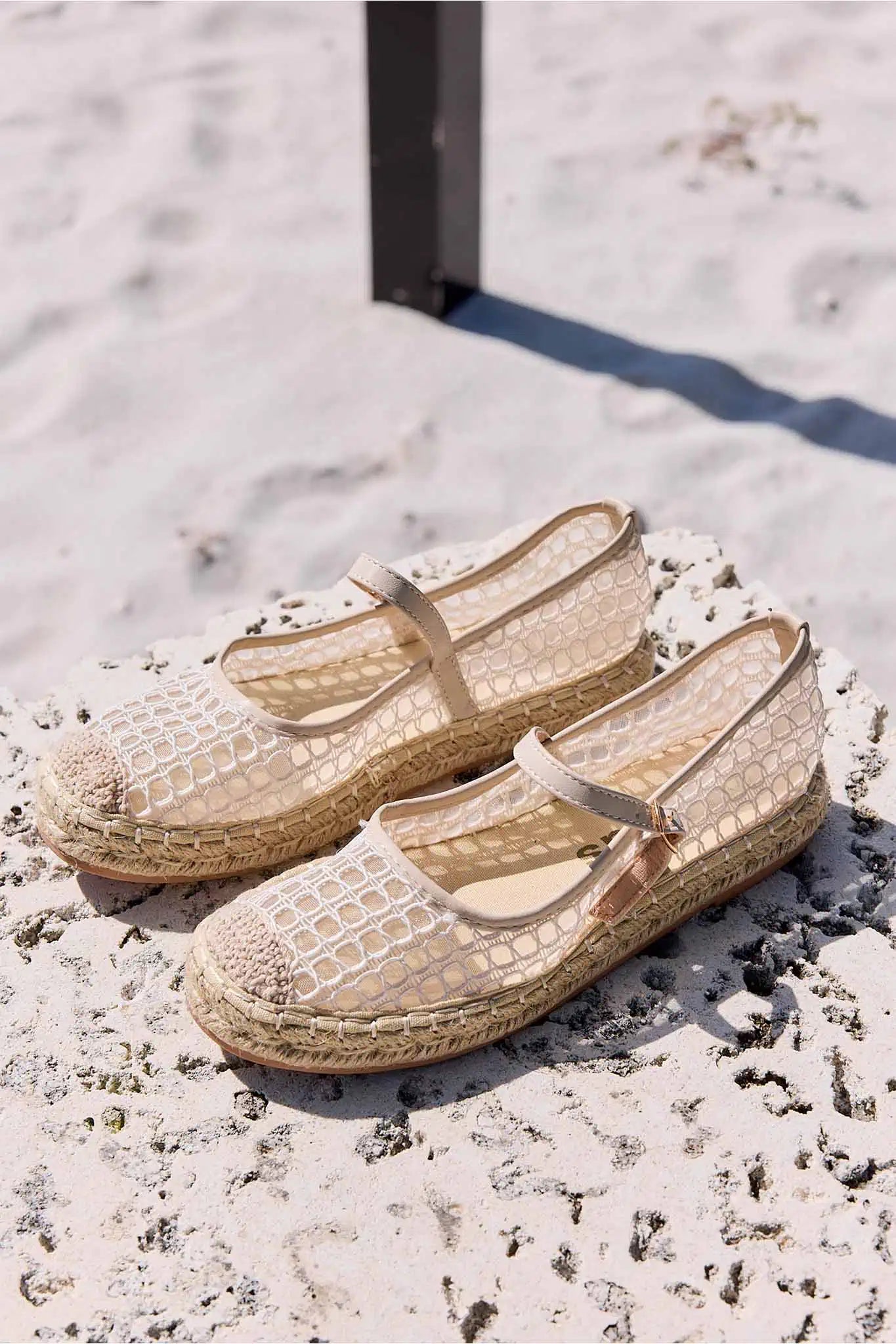 Pair of beige espadrille shoes on a sandy surface