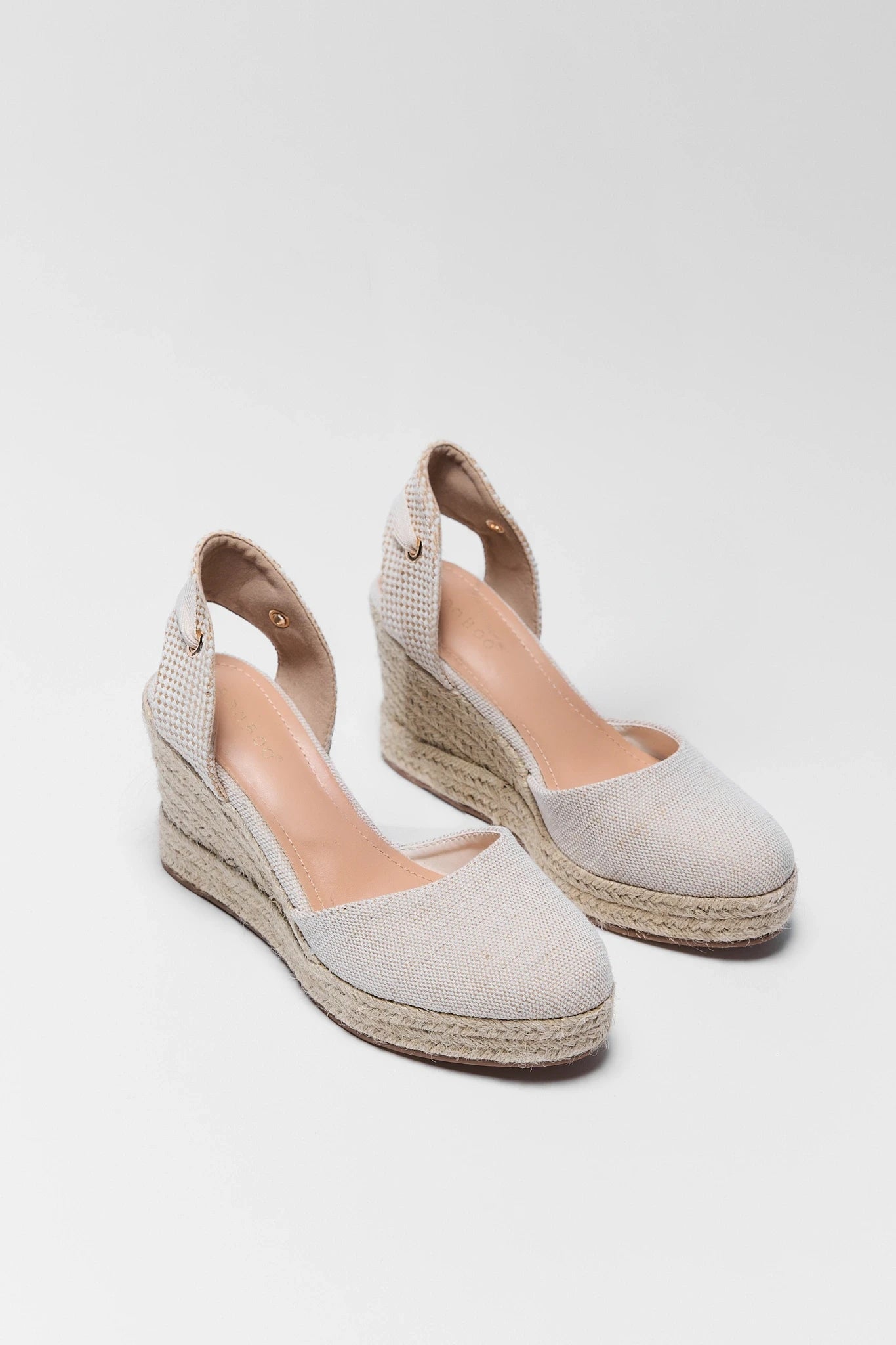 Pair of beige wedge sandals with espadrille sole on a white background