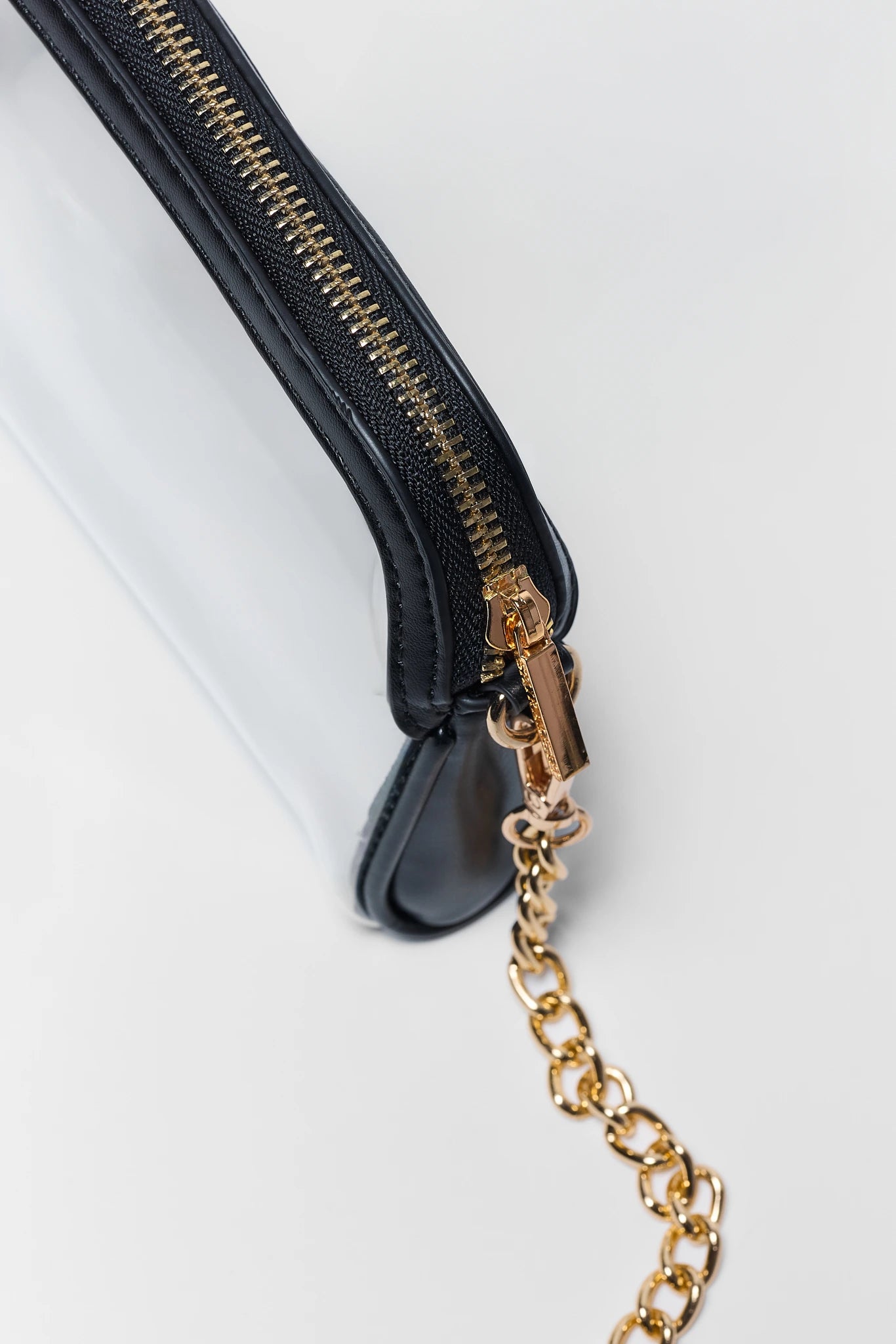 Close-up of a black leather wristlet pouch with a gold zipper and a gold chain link accent, shown on a clean white background.