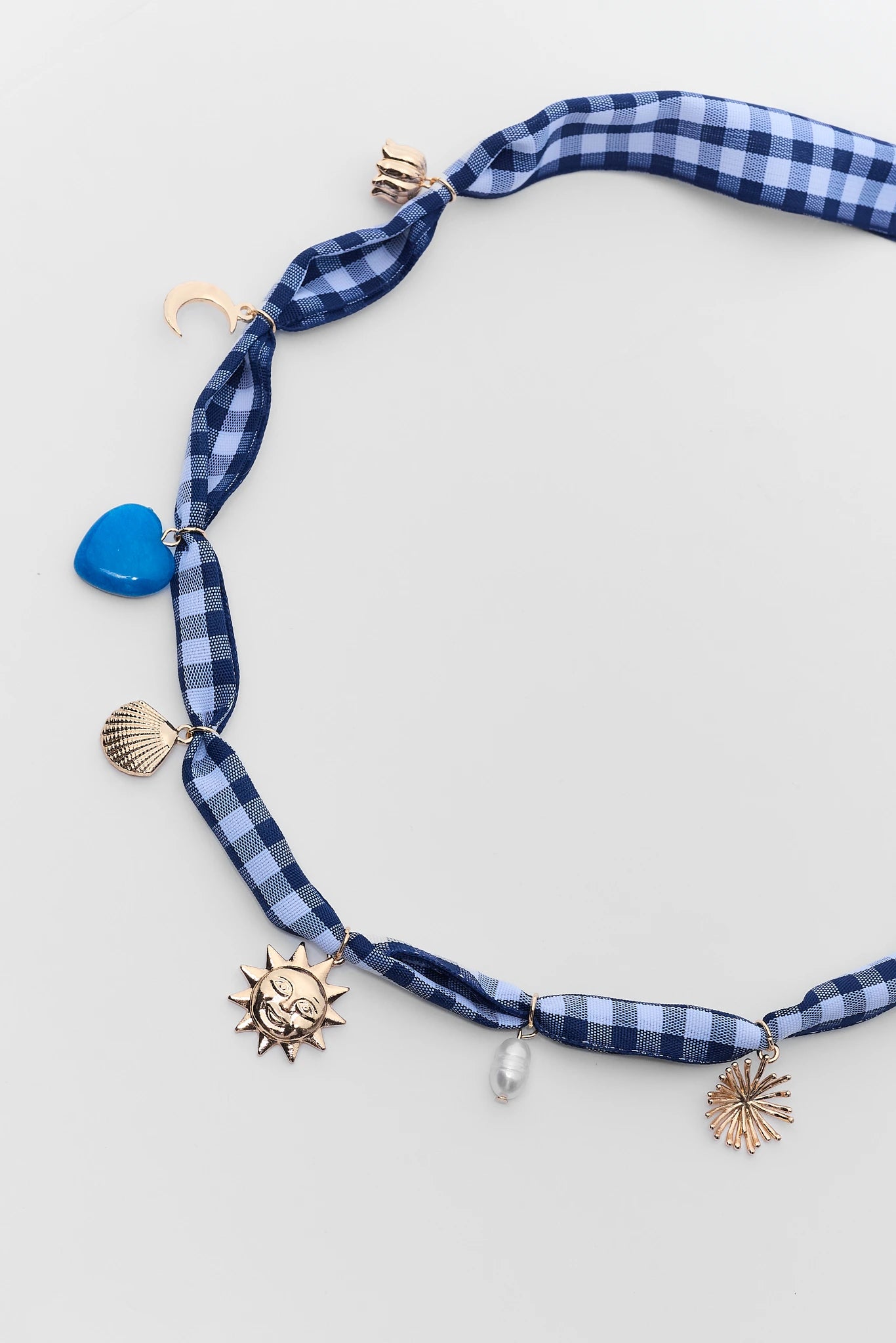 close up Necklace with blue checkered ribbon, blue heart charm, sun charm, and shell charms on a light gray background