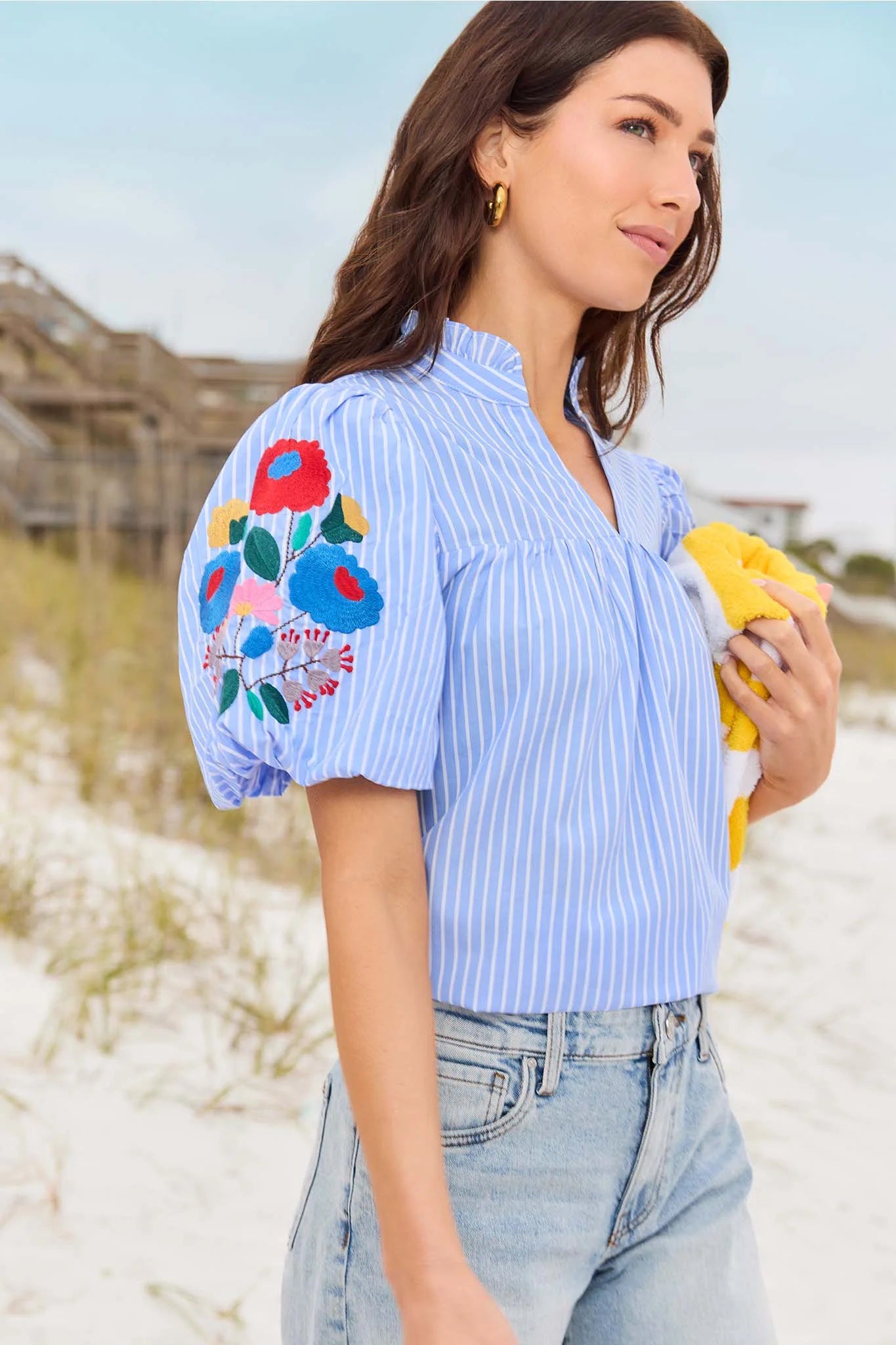 Woman wearing a blue striped shirt with floral embroidery on the sleeves at the beach.