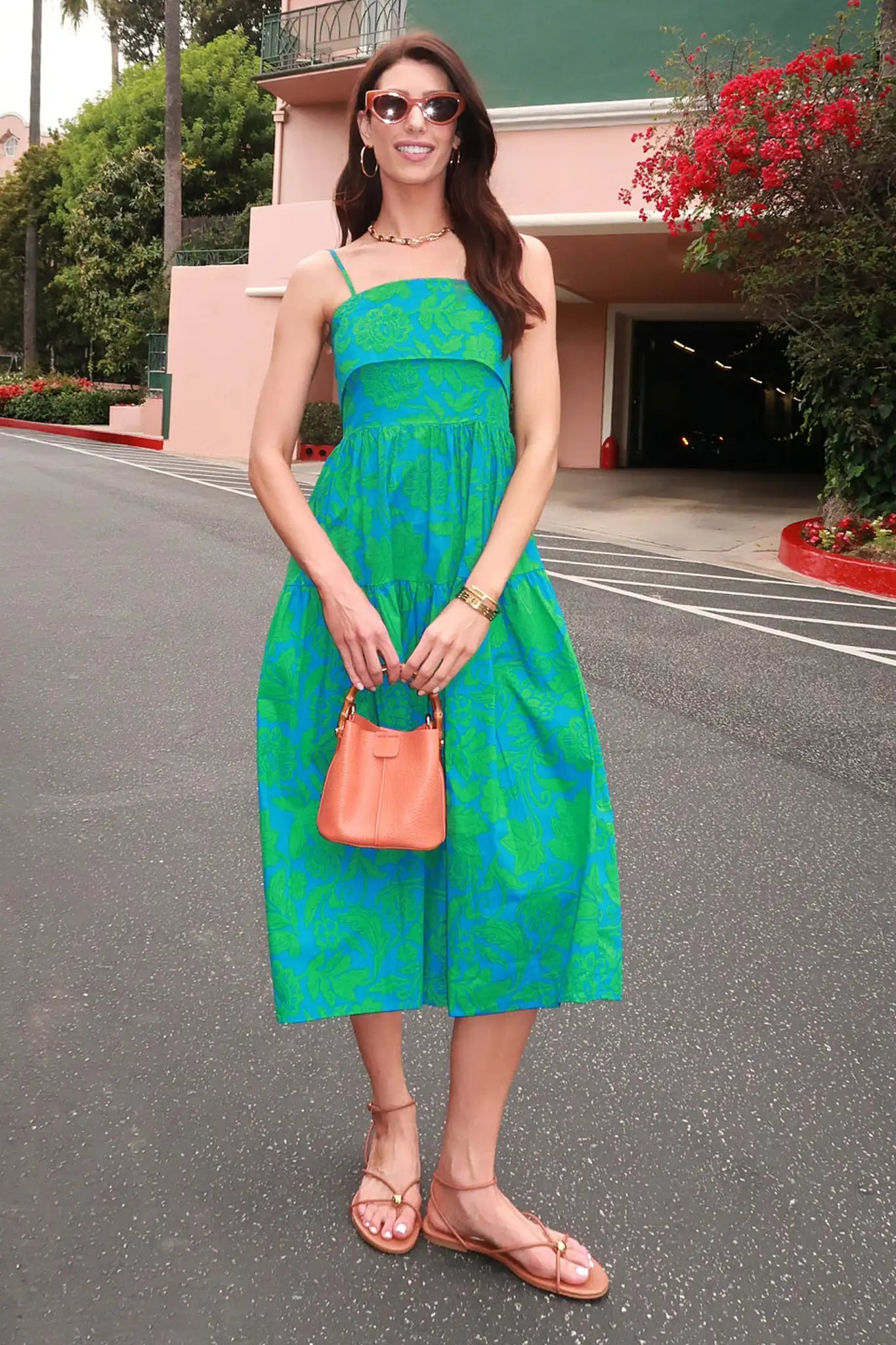 Woman in a green dress holding an orange handbag on a street.