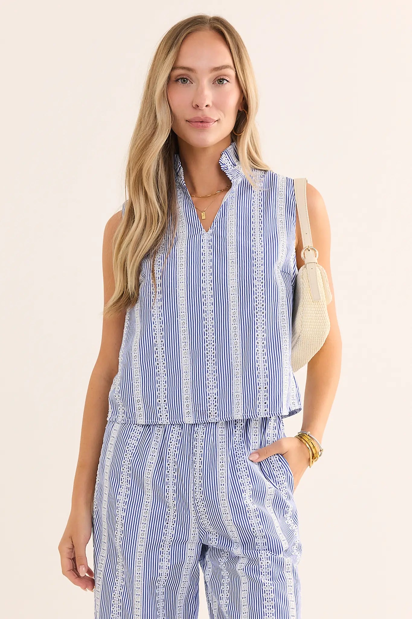 Woman wearing a blue and white striped sleeveless top and pants against a plain background