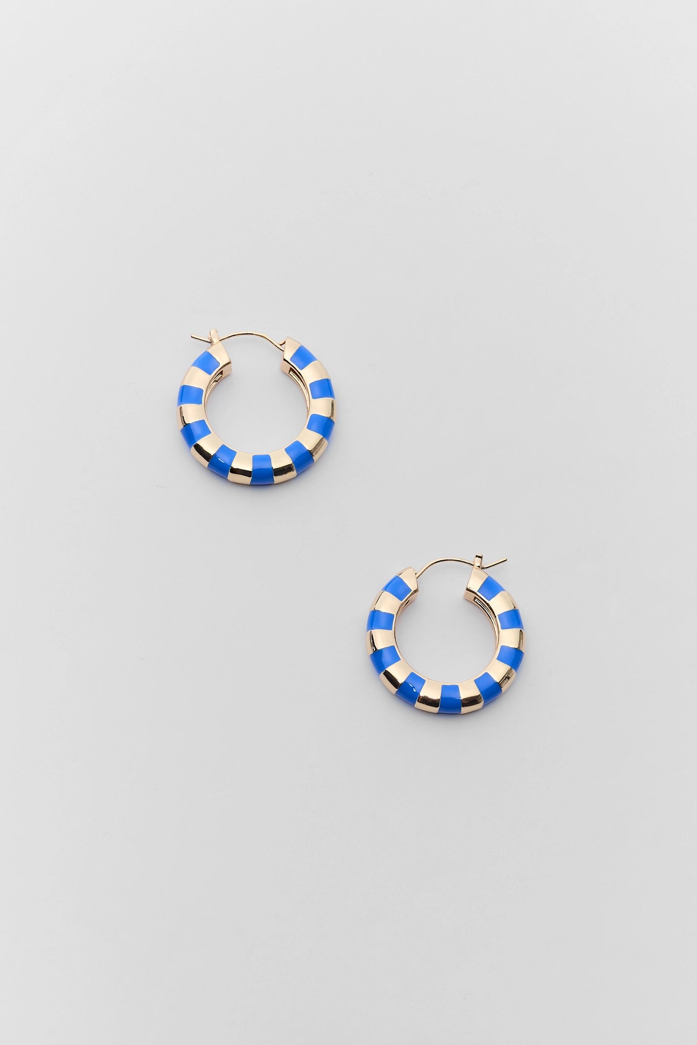 A pair of gold hoop earrings with a blue and white striped enamel pattern, displayed on a light gray background.