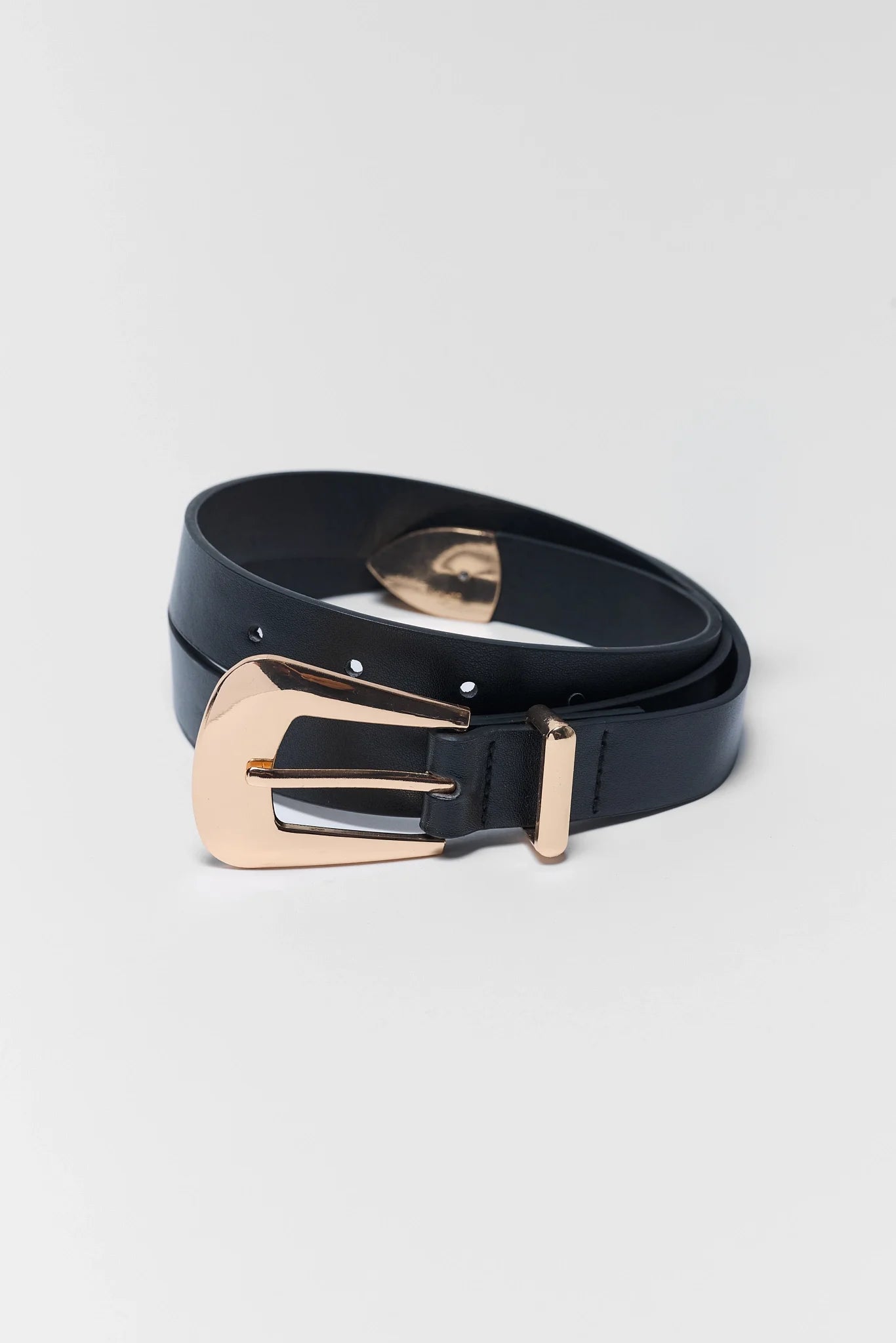 A black leather belt with a large, polished rose gold buckle, coiled on a light gray background.