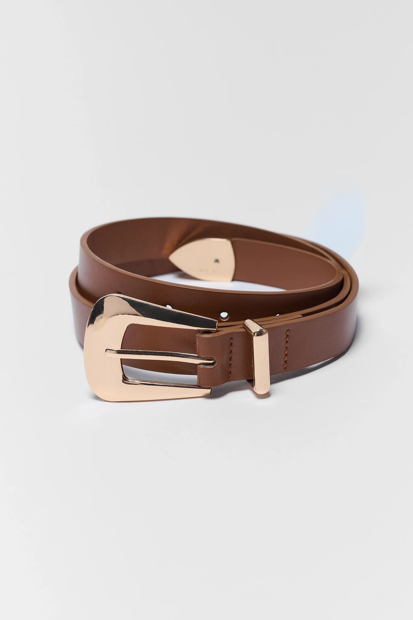 A brown leather belt with a polished rose gold buckle, neatly coiled on a light gray background.