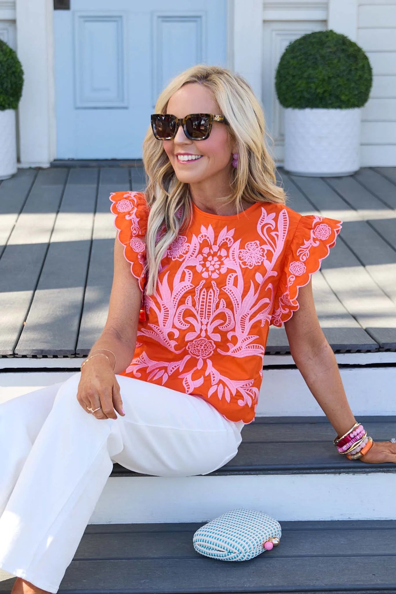 Woman wearing an orange and pink patterned top sitting on a wooden deck.