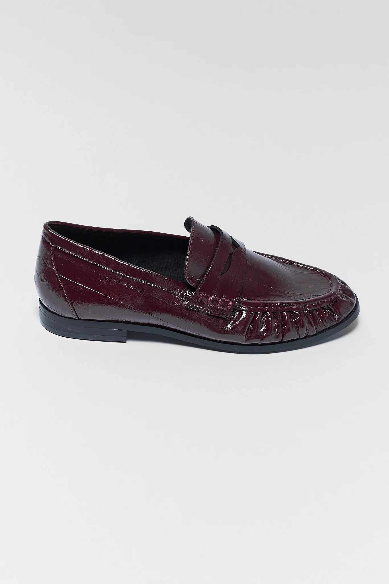 A single dark burgundy leather penny loafer shown from a side profile view against a light gray background.
