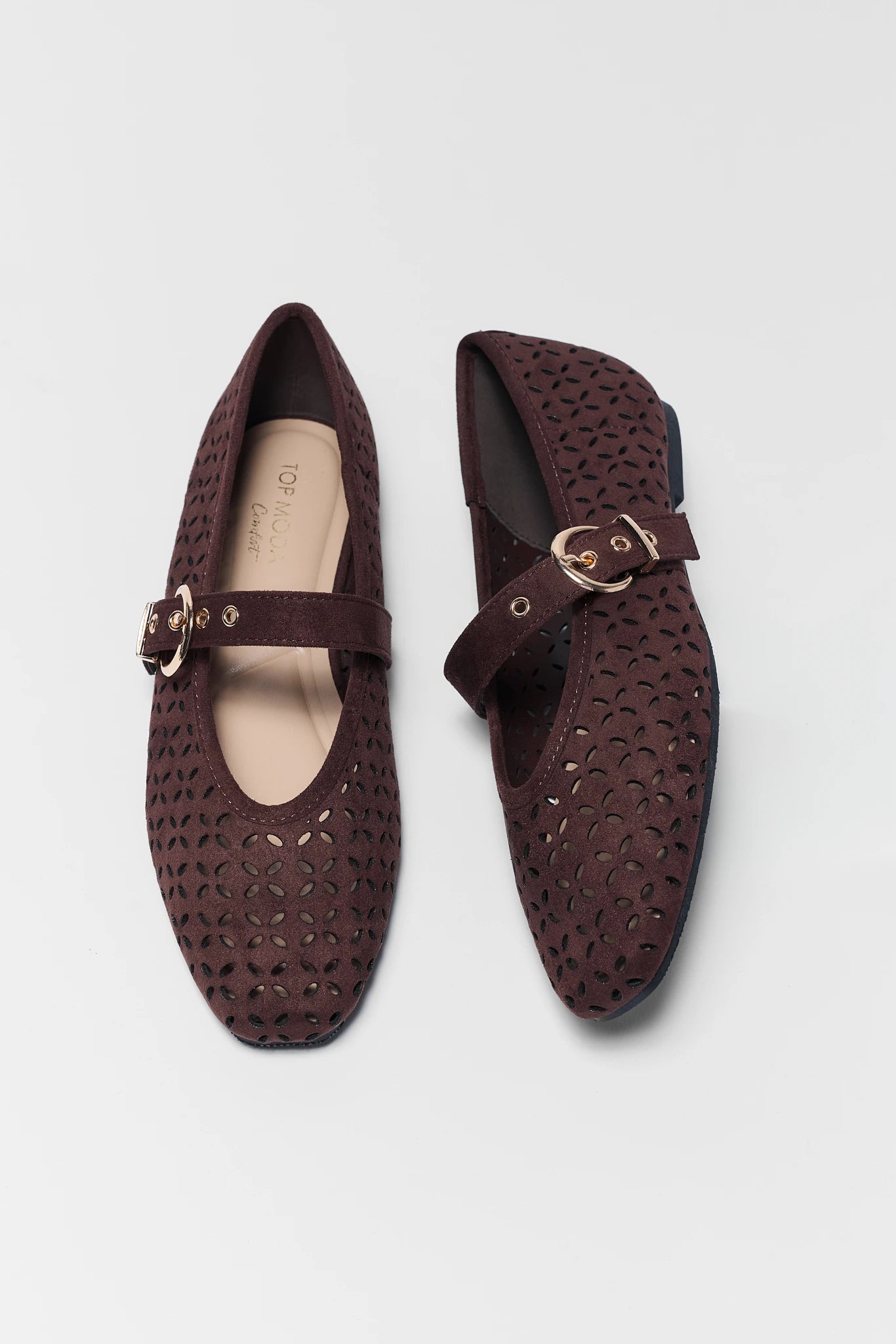 A pair of dark brown leather flat shoes with an intricate laser-cut geometric pattern, featuring a single strap with a gold-tone buckle on a light gray background.