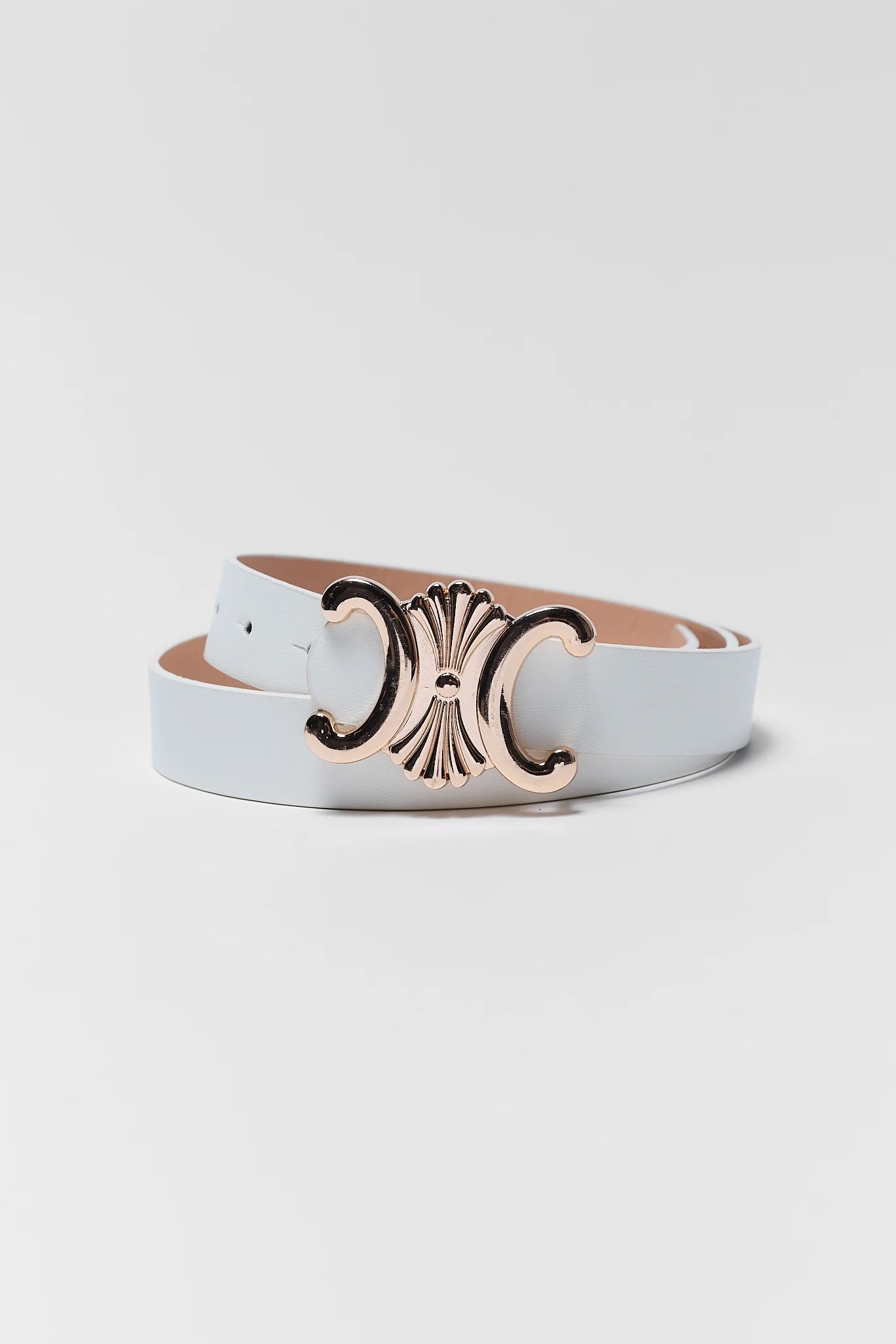 A white leather belt with a large, ornate metallic C-shaped buckle in a rose gold finish, coiled on a light gray background.