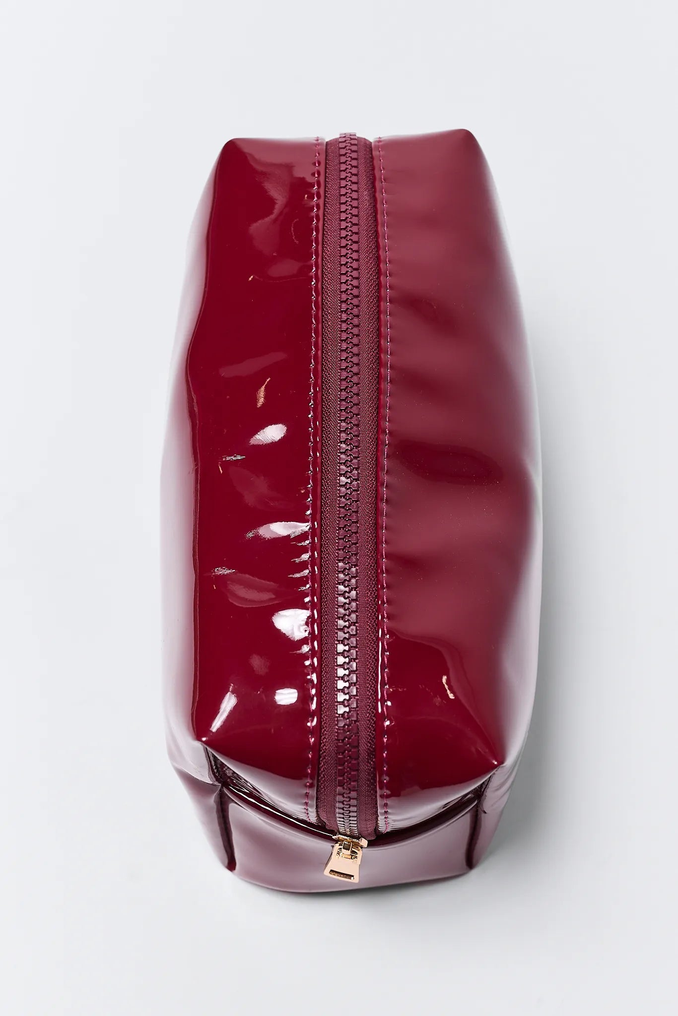 Red patent leather pouch with gold zipper on a white background