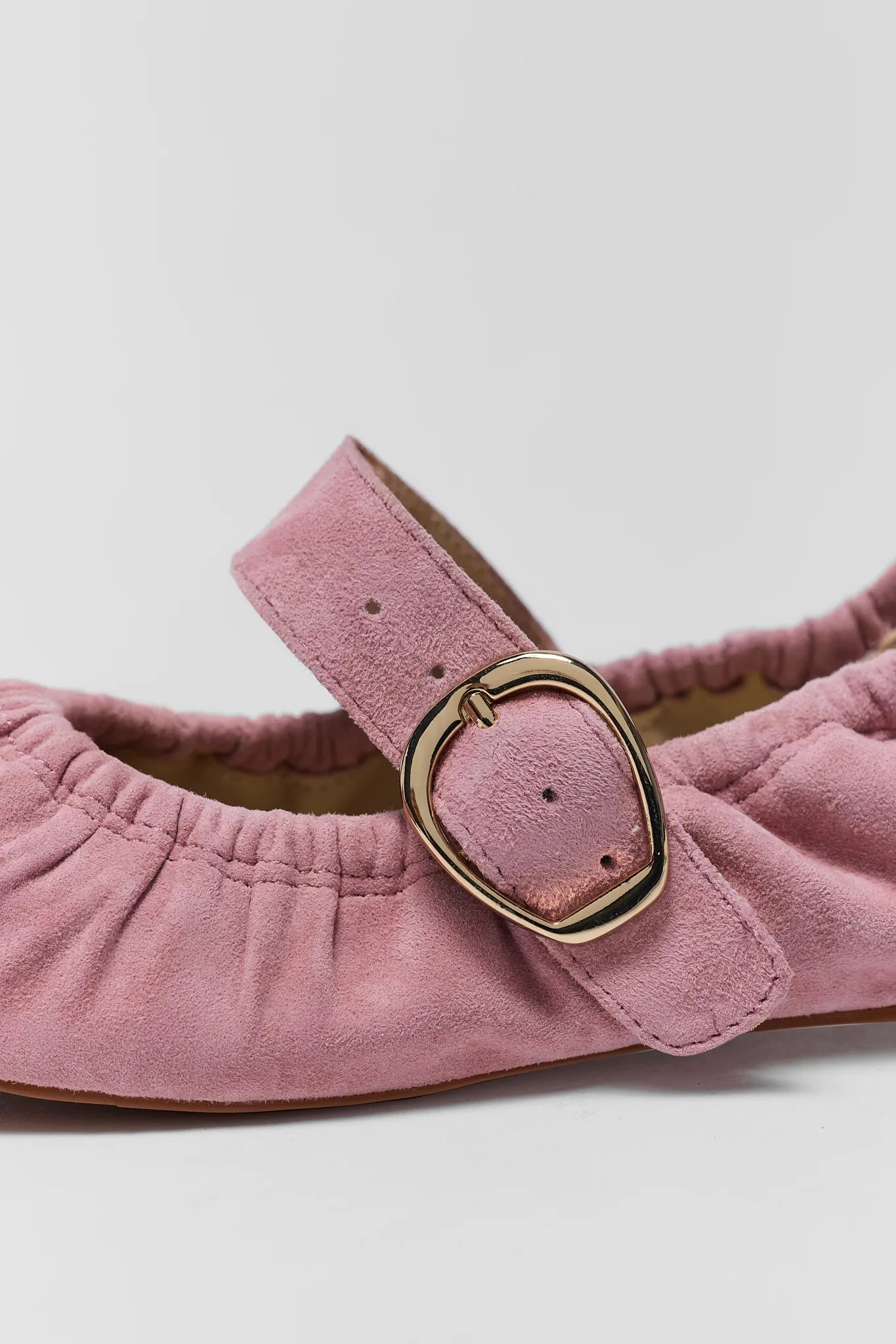 Pink suede sandal with a gold buckle on a light gray background