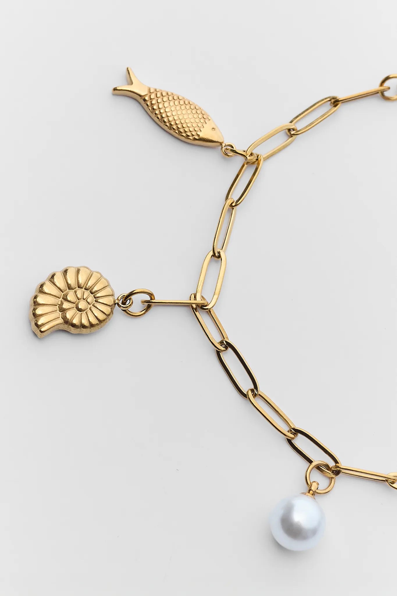 Gold necklace with seashell and pearl charms on a light gray background