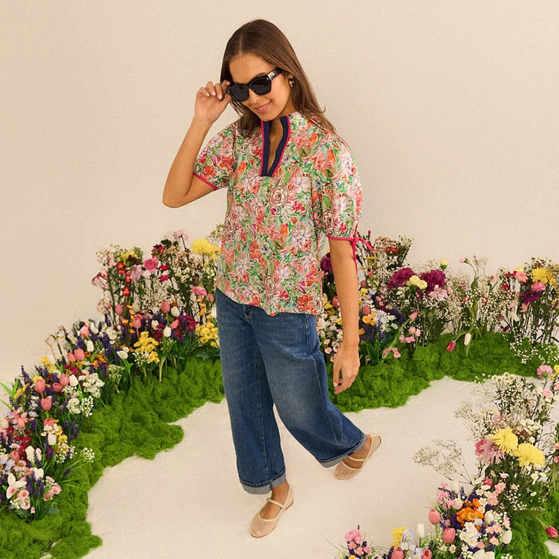 Woman in a floral shirt and jeans standing in front of a flower garden