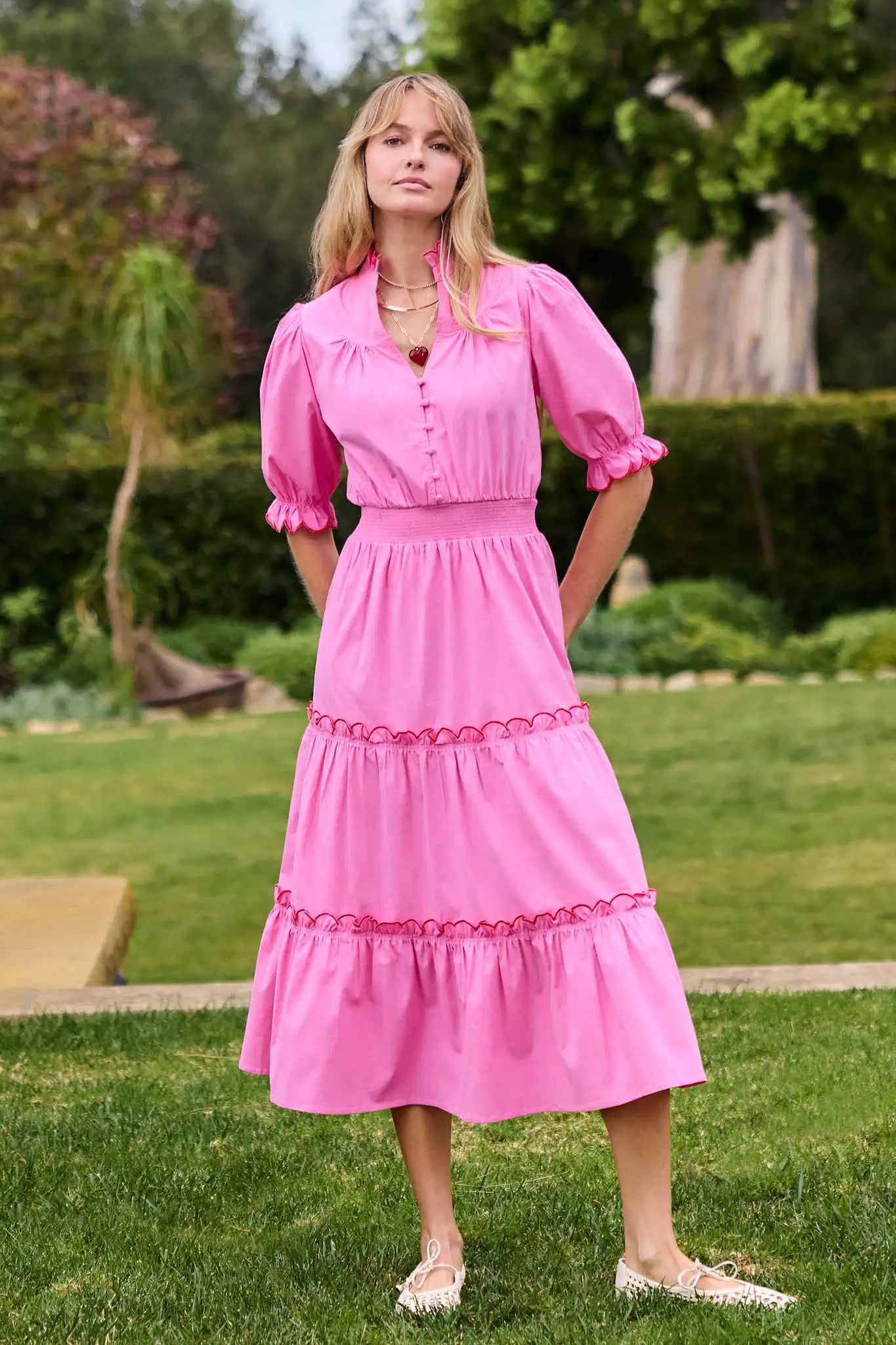 Woman wearing a pink dress standing outdoors in a garden setting