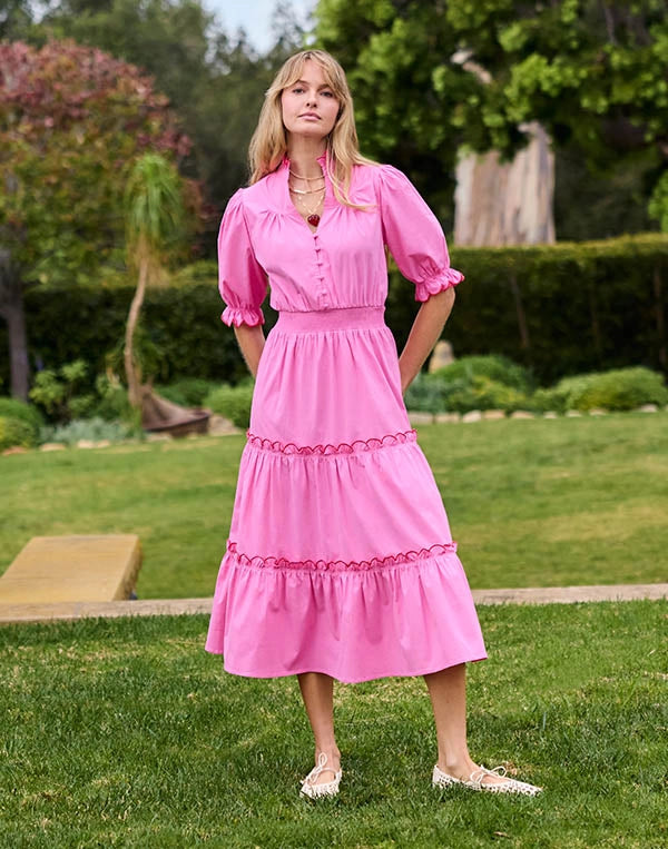Woman in a pink dress standing on grass with trees in the background