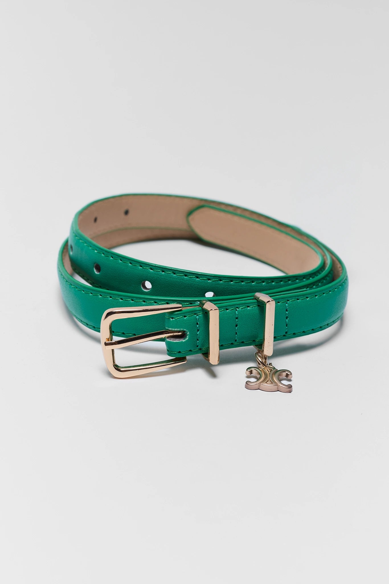 A green leather belt with a gold-tone buckle and a small hanging charm, coiled on a light gray background.