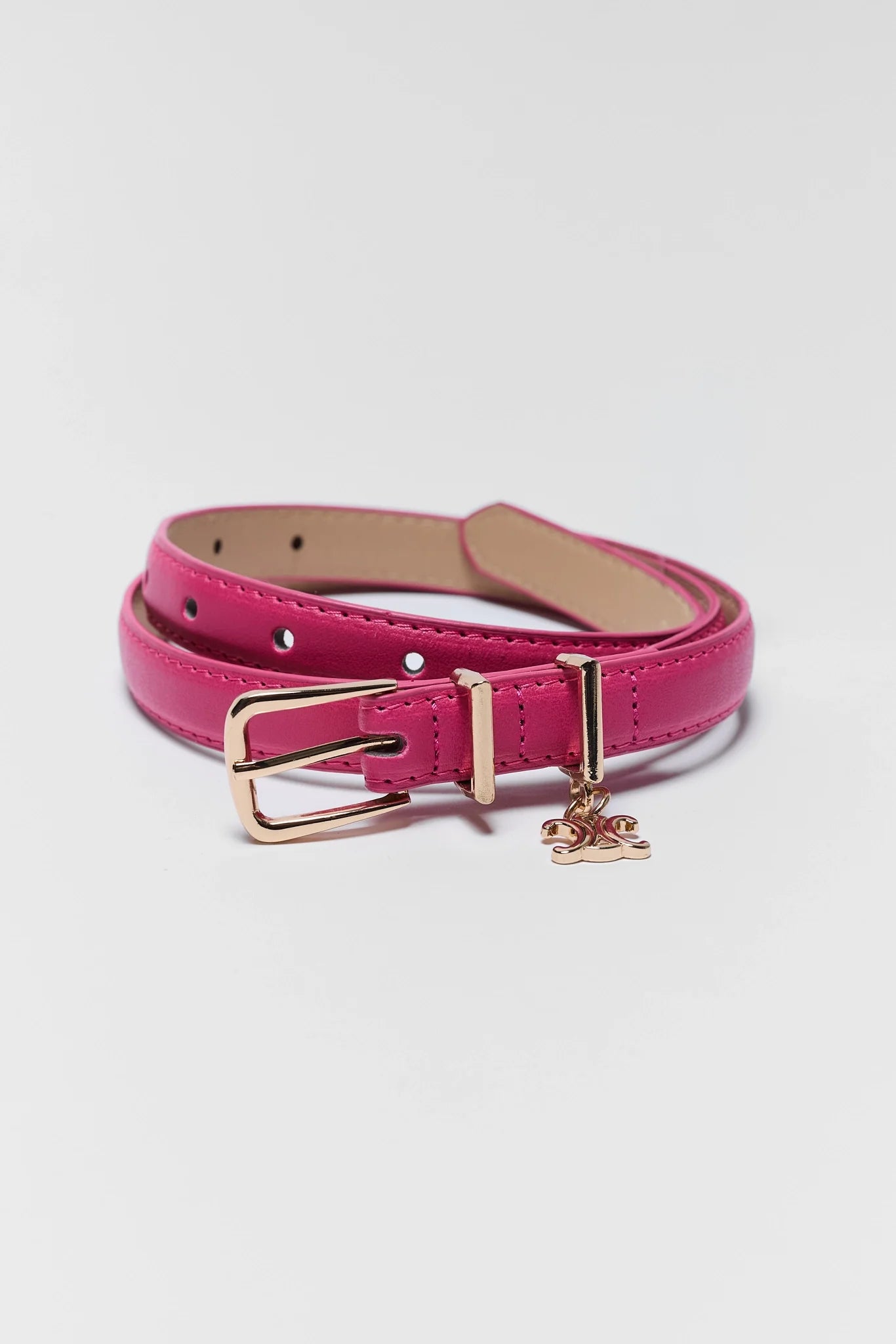 A bright pink faux leather belt with a gold-tone buckle and a small hanging horse charm, coiled on a light gray background.