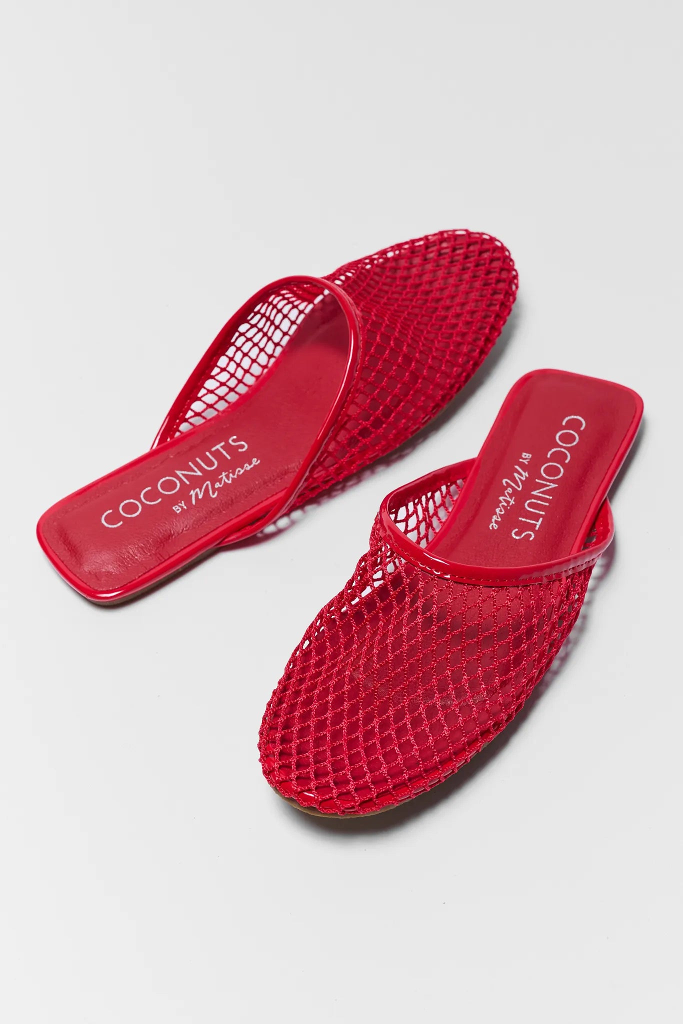 Red mesh sandals with 'Coconuts by Milo' branding on a light gray background