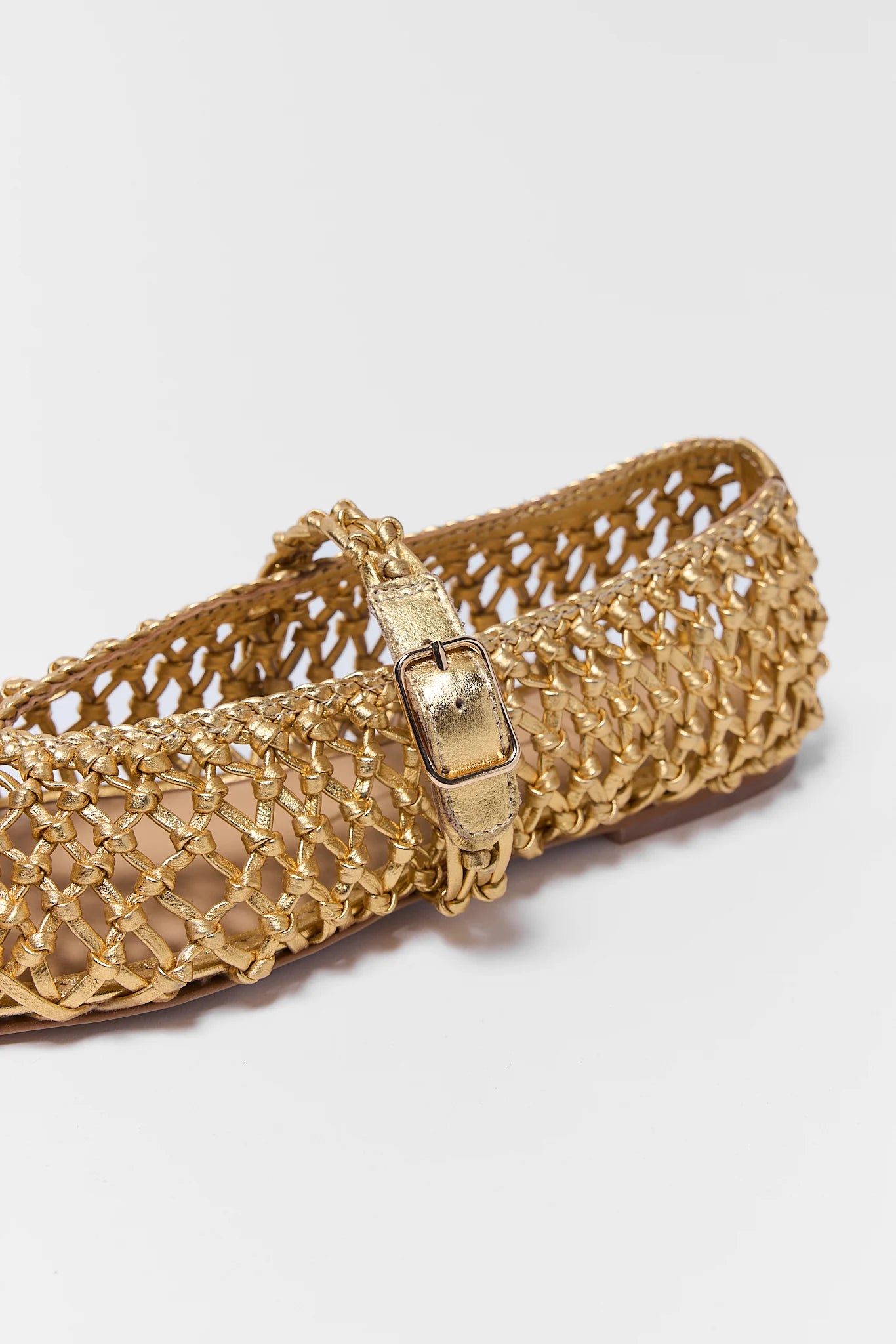 Gold woven flat shoe on a light gray background close up