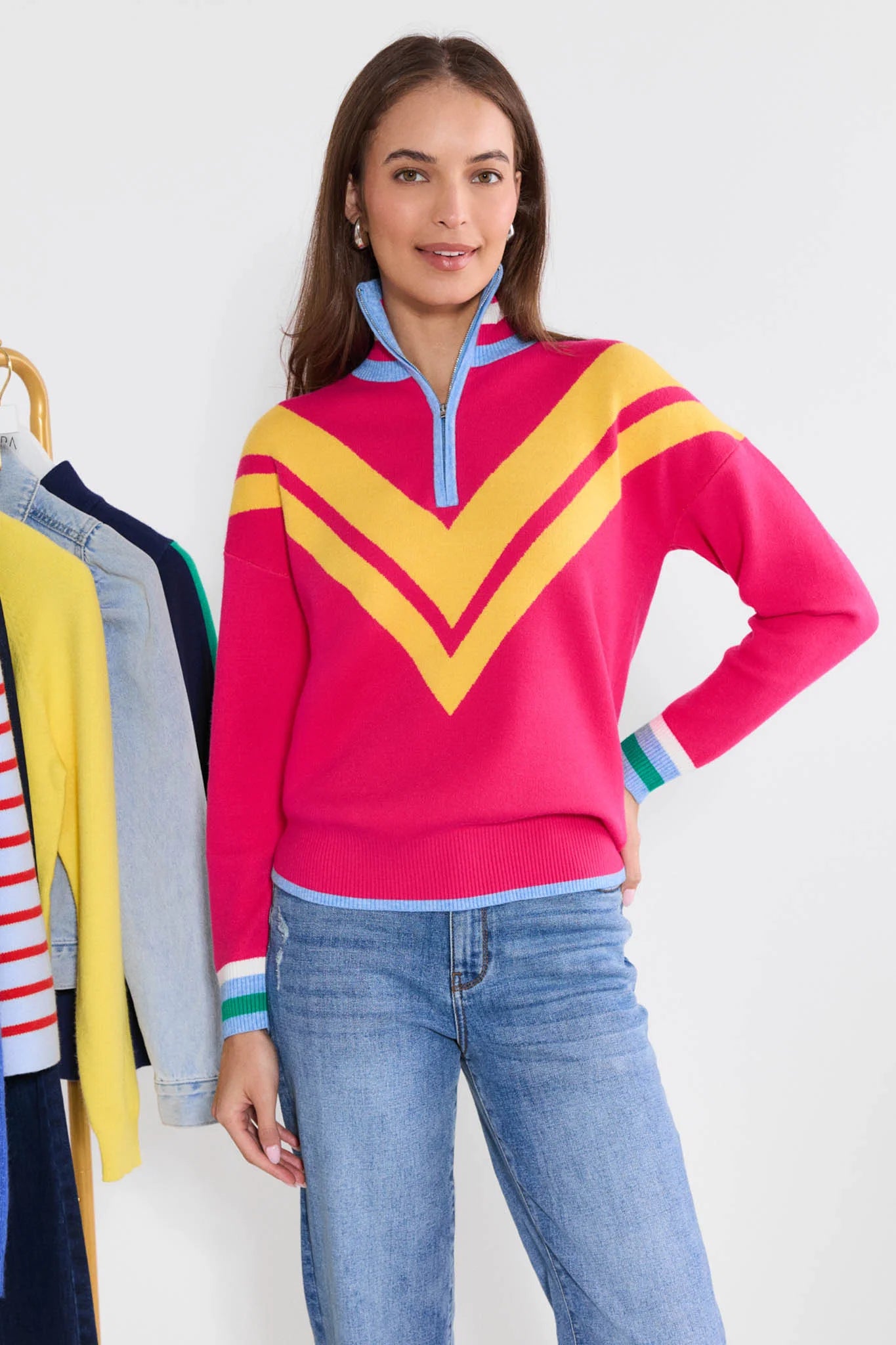 Woman wearing a colorful sweater with a yellow and pink design, standing in front of a white background.