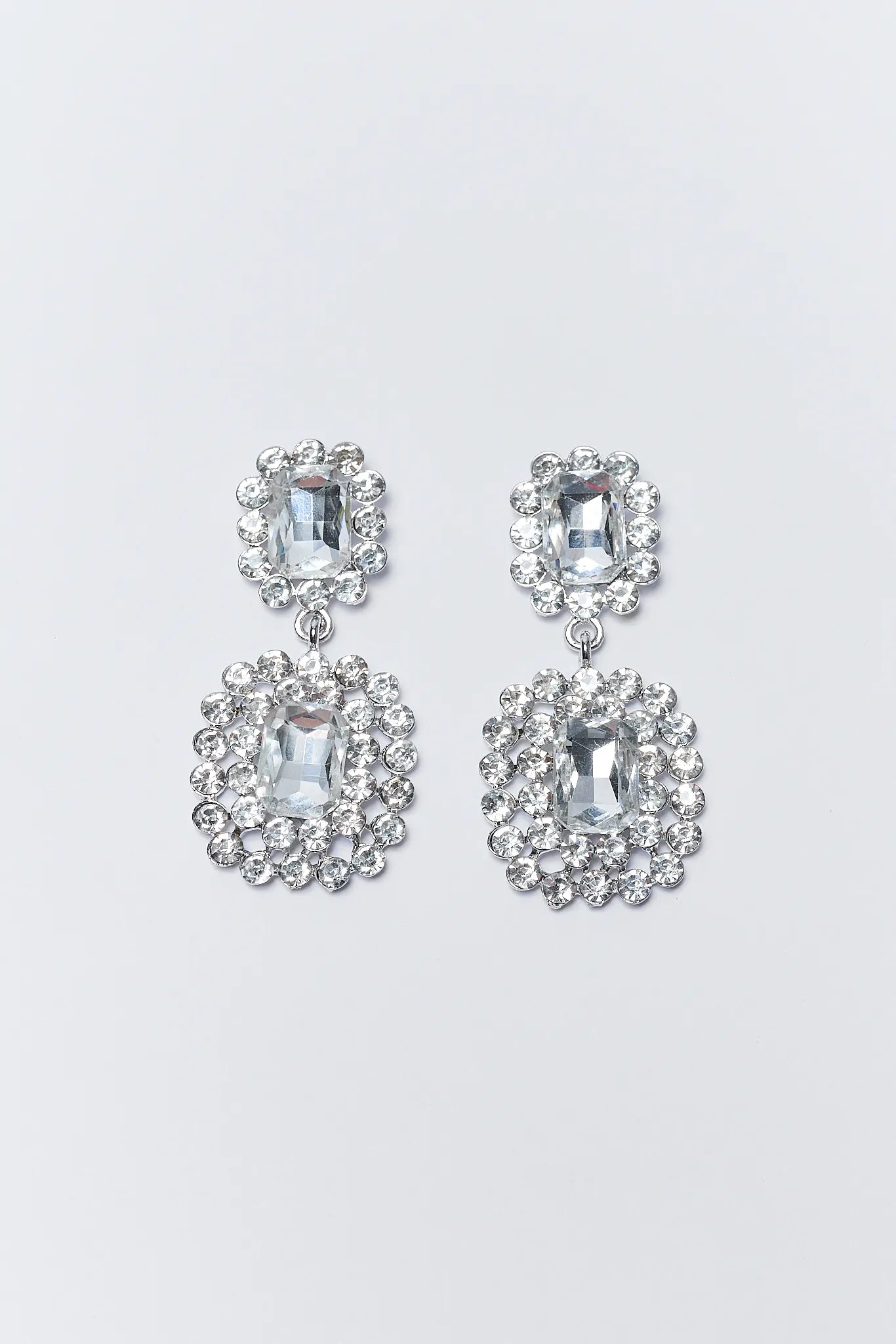 Pair of silver earrings with clear gemstones on a light gray background