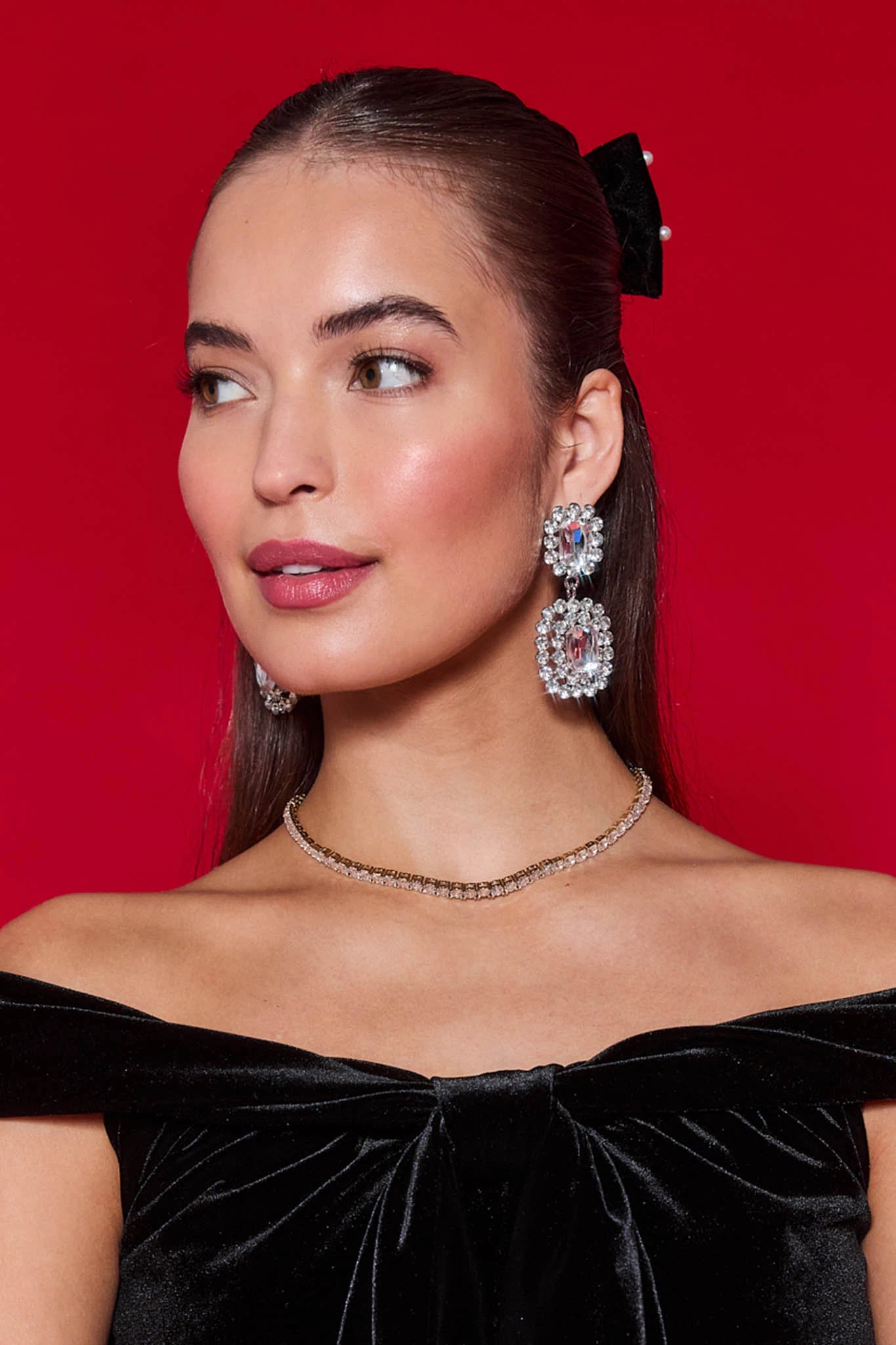 Woman wearing a black off-shoulder top with jewelry against a red background