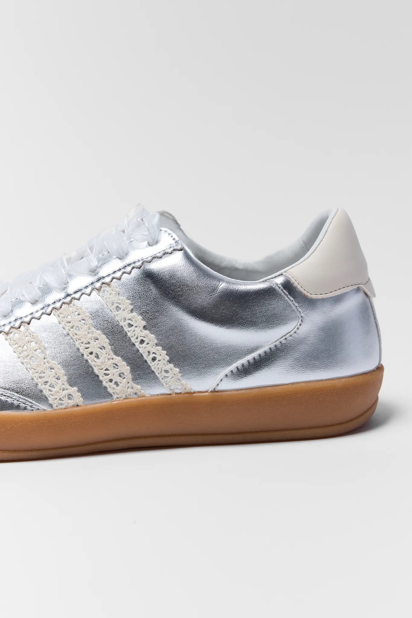 close up of silver sneakers with lace details and ribbon on white background