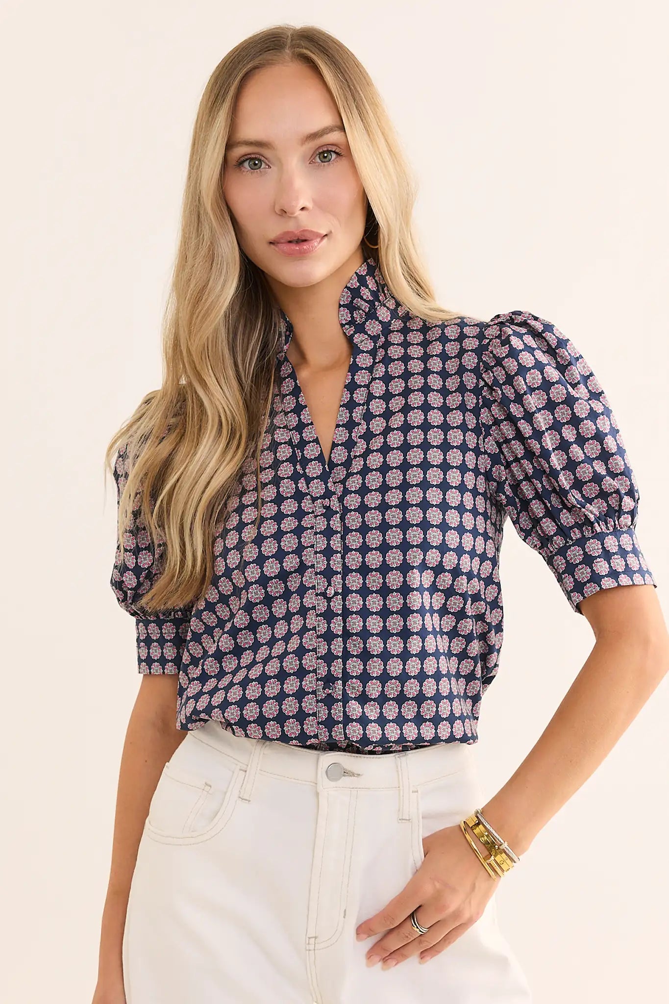 Woman wearing a geometric navy and purple top with white jeans on a cream background