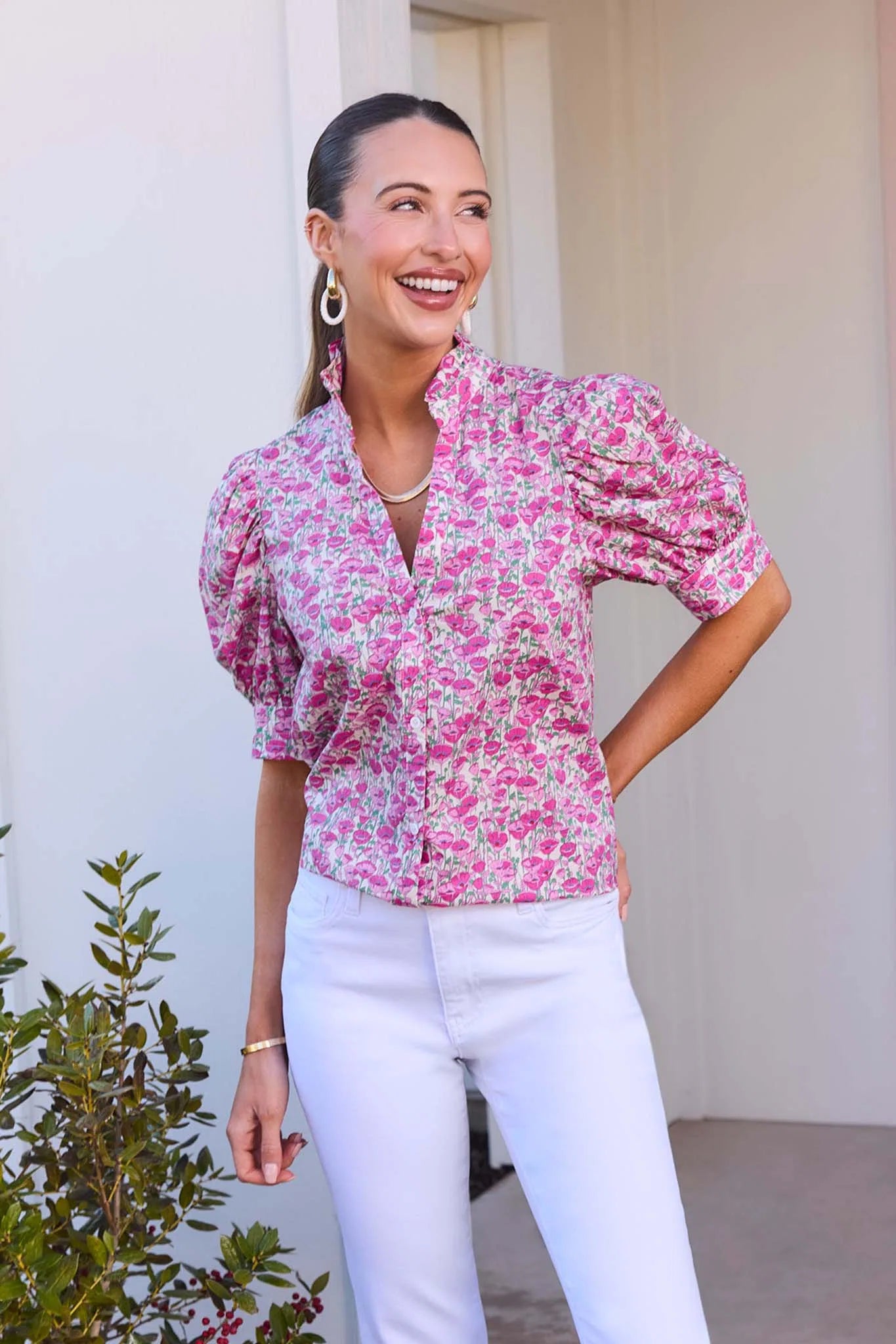 Woman wearing a pink floral blouse and white pants standing outdoors.
