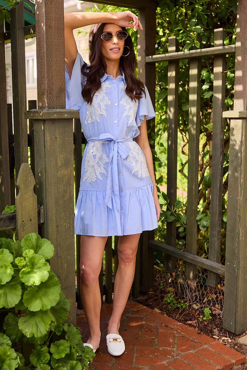 Woman wearing a light blue dress with floral patterns in an outdoor setting.