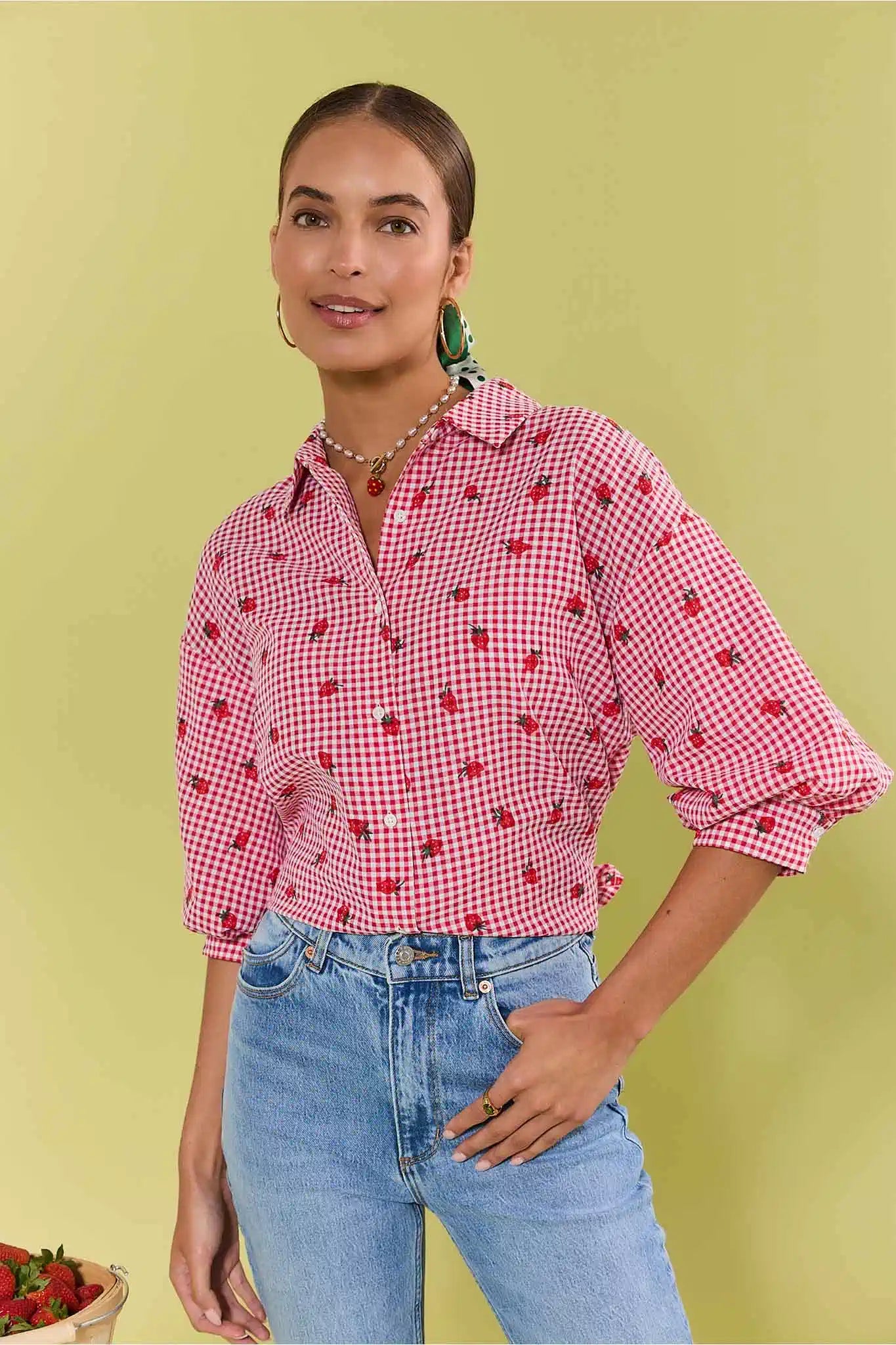 Woman wearing a red and white checkered shirt with strawberry pattern against a light green background