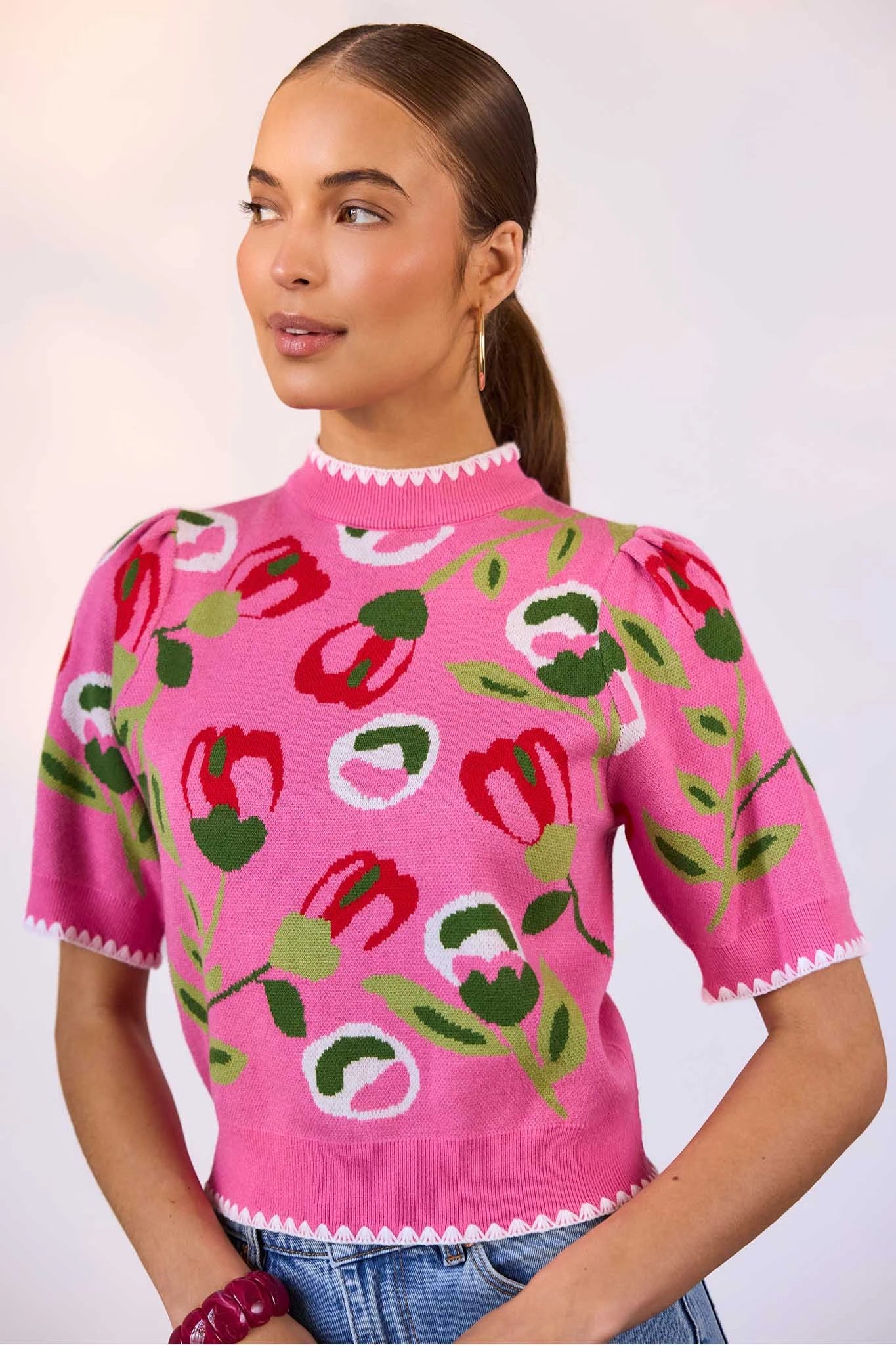 Woman wearing a pink sweater with floral patterns on a plain background