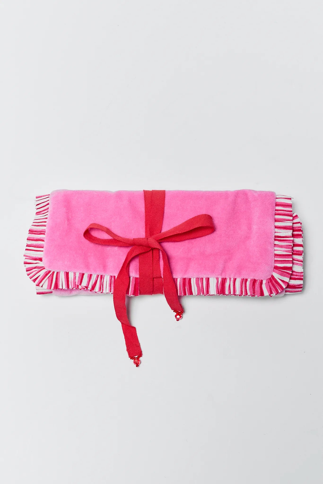 Pink baby blanket with ruffles and a red ribbon on a light gray background