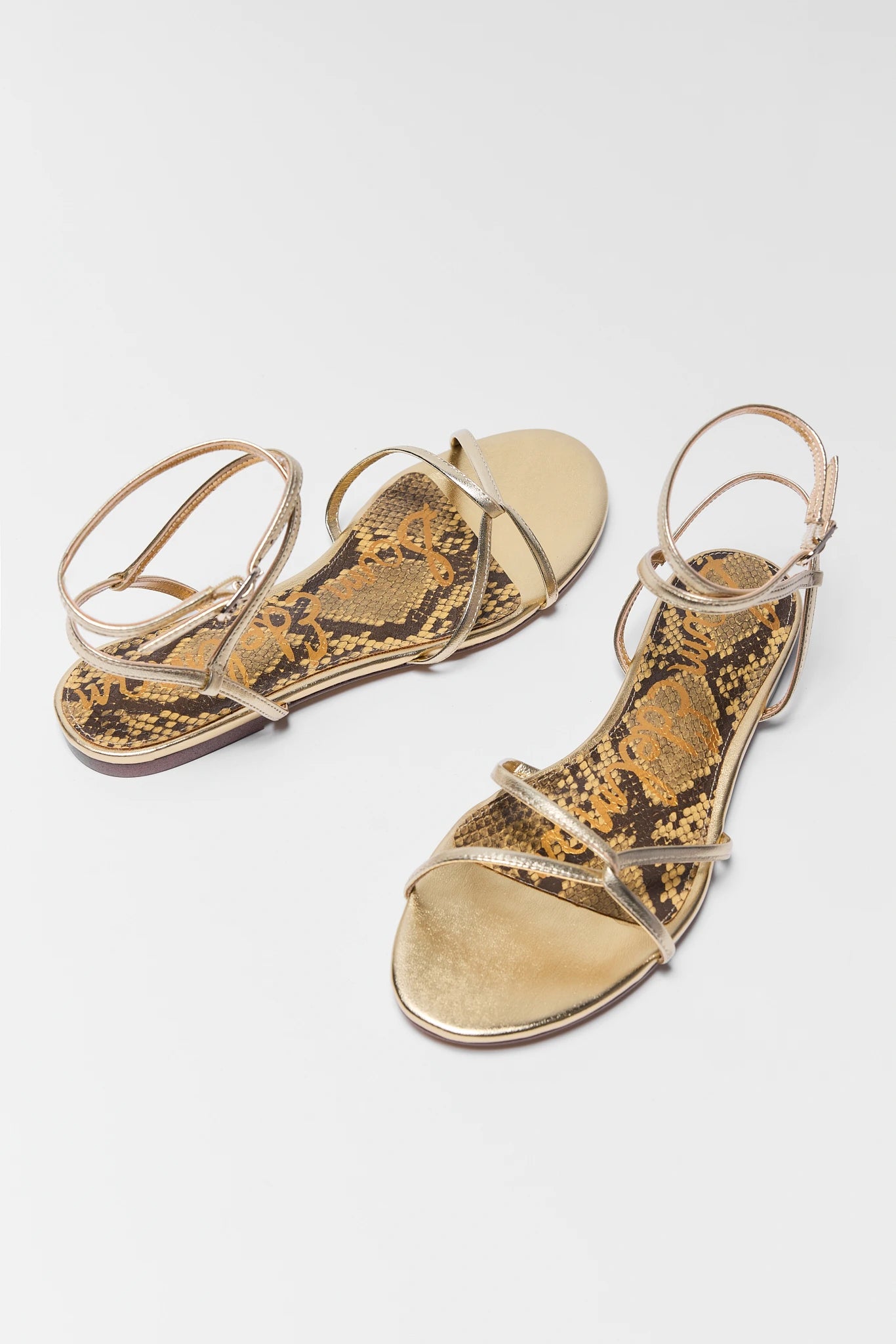 Pair of gold sandals with snake print on a white background