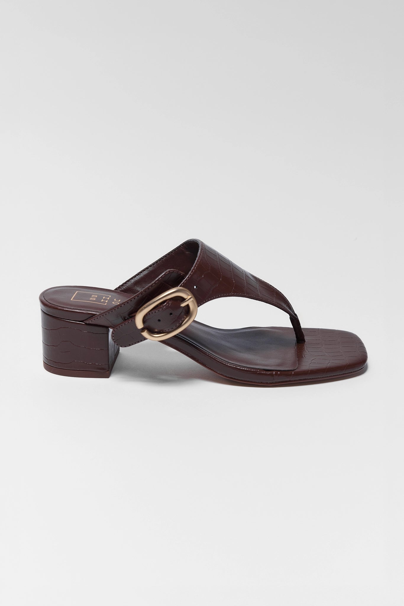 Brown sandal with a gold buckle on a light gray background