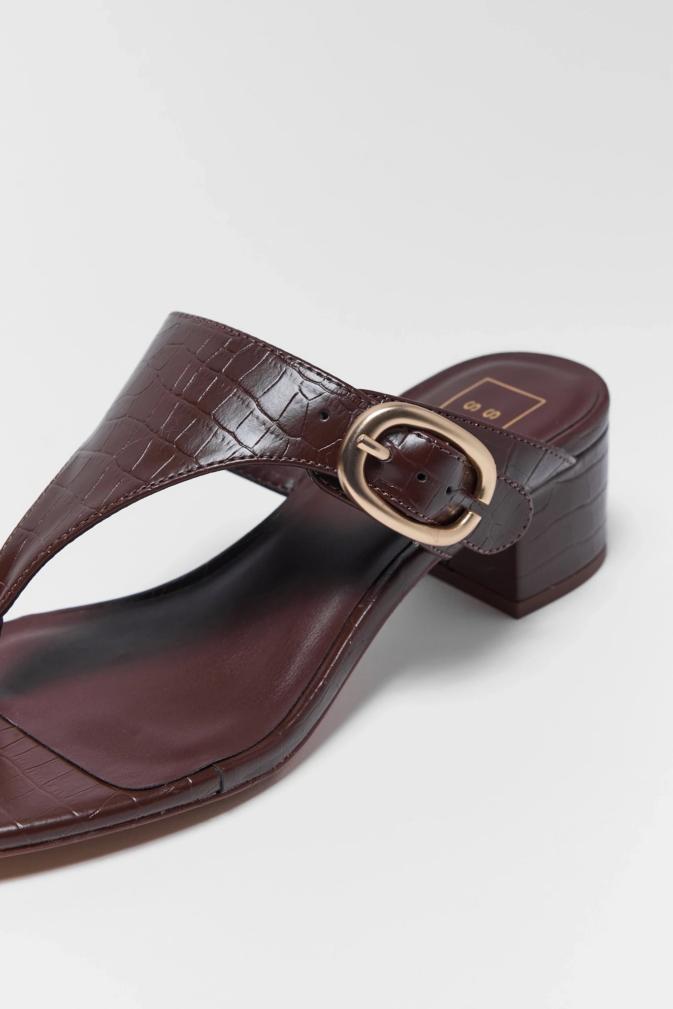 Brown sandal with a gold buckle on a light gray background close up