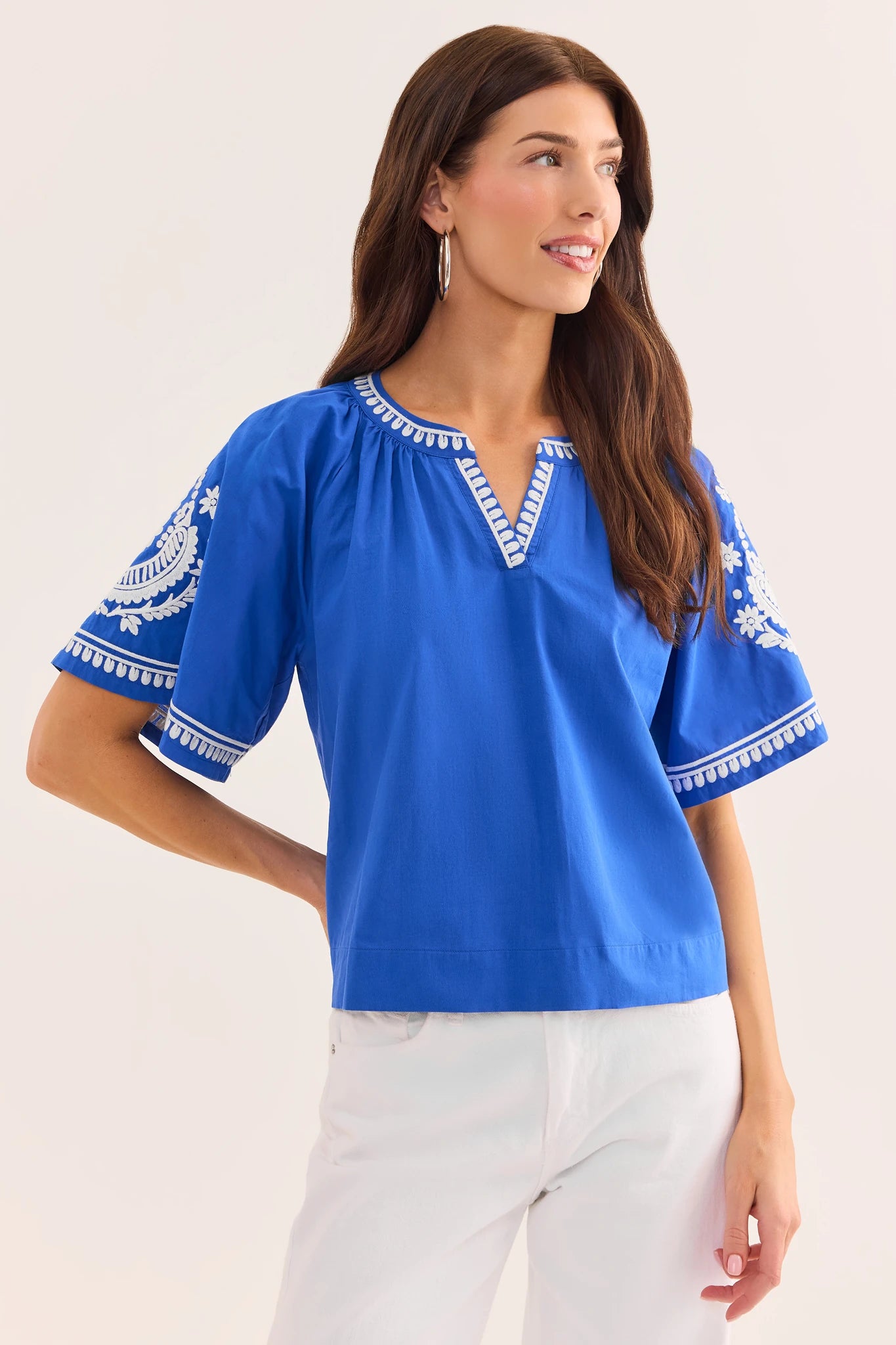 Woman wearing a blue blouse with white embroidery on a plain background