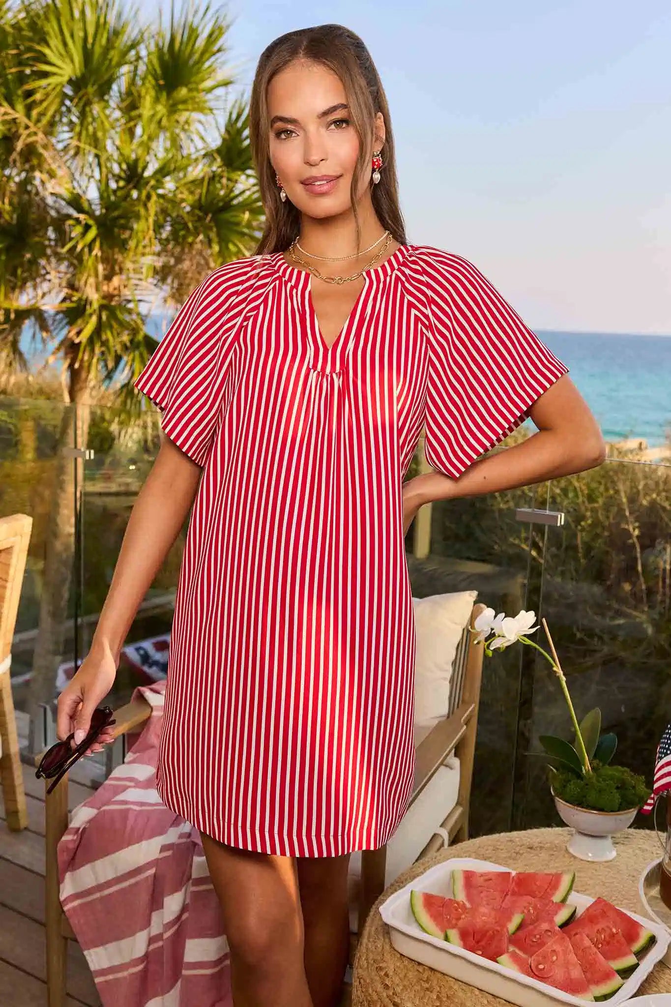 Woman in a red and white striped dress standing by a table with watermelon slices, outdoor setting.
