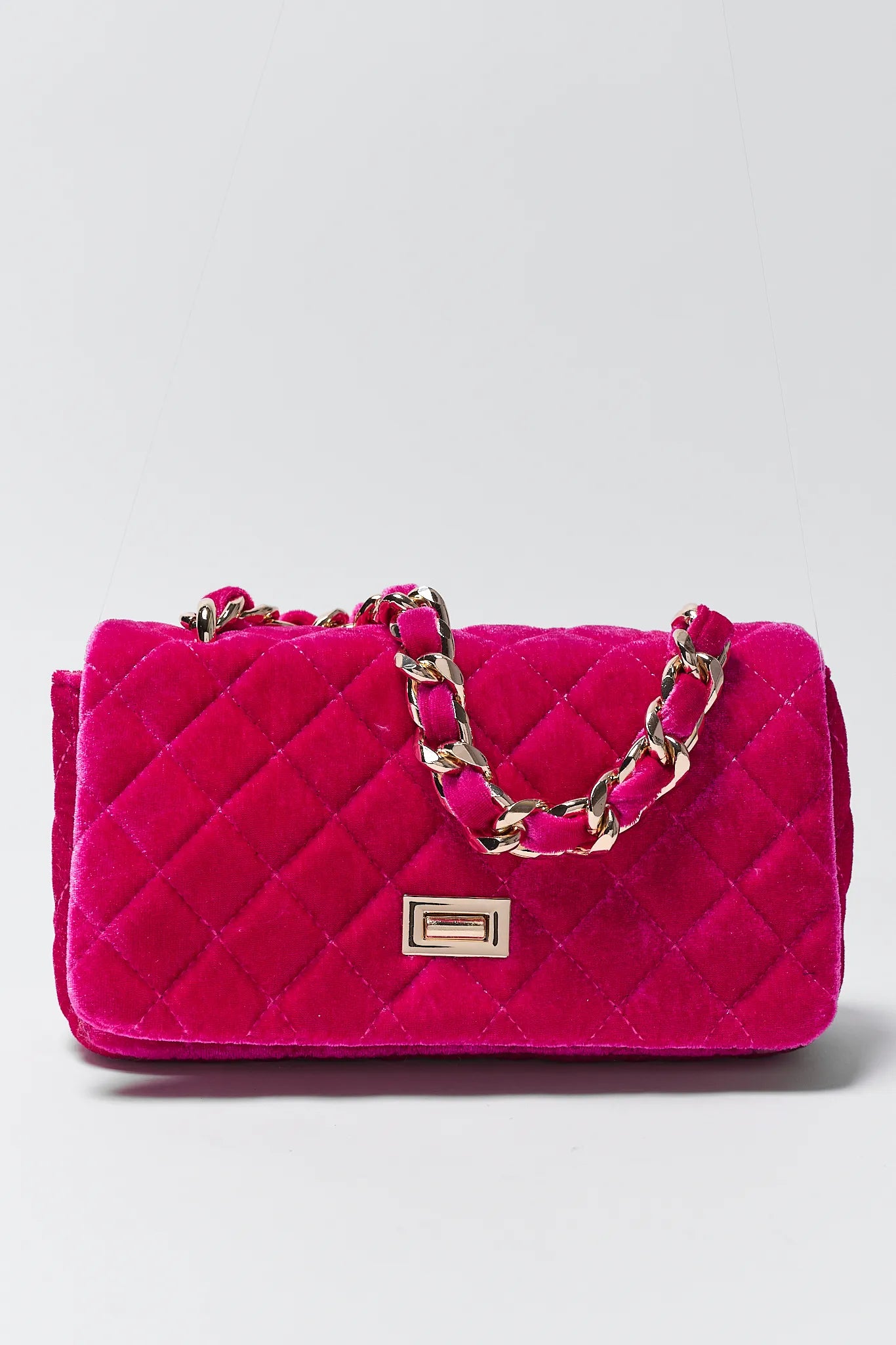 Pink quilted handbag with gold chain strap on a light gray background