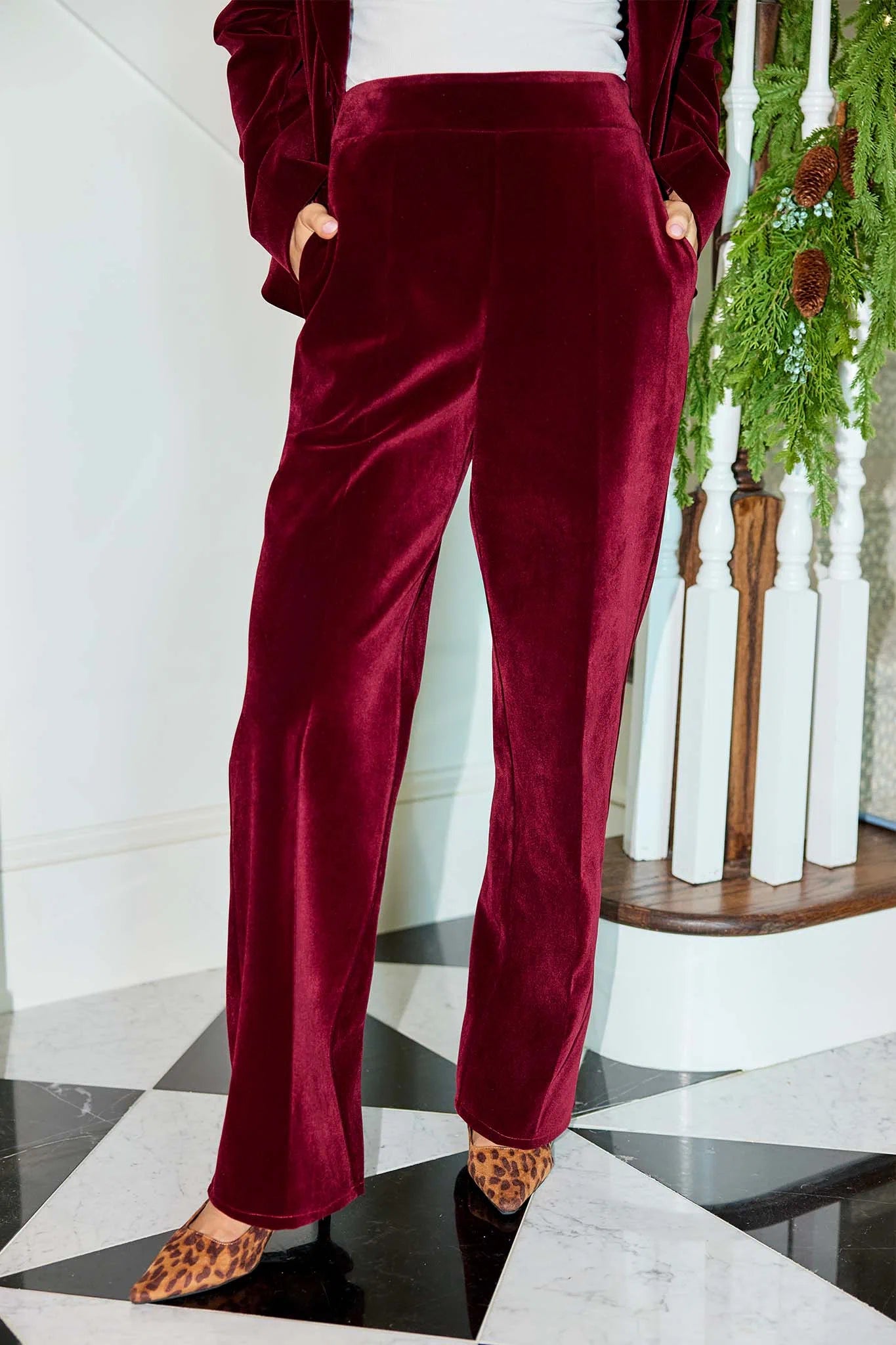 Person wearing Evie Cranberry Velvet Pants with a white marble floor and decorative plant in the background