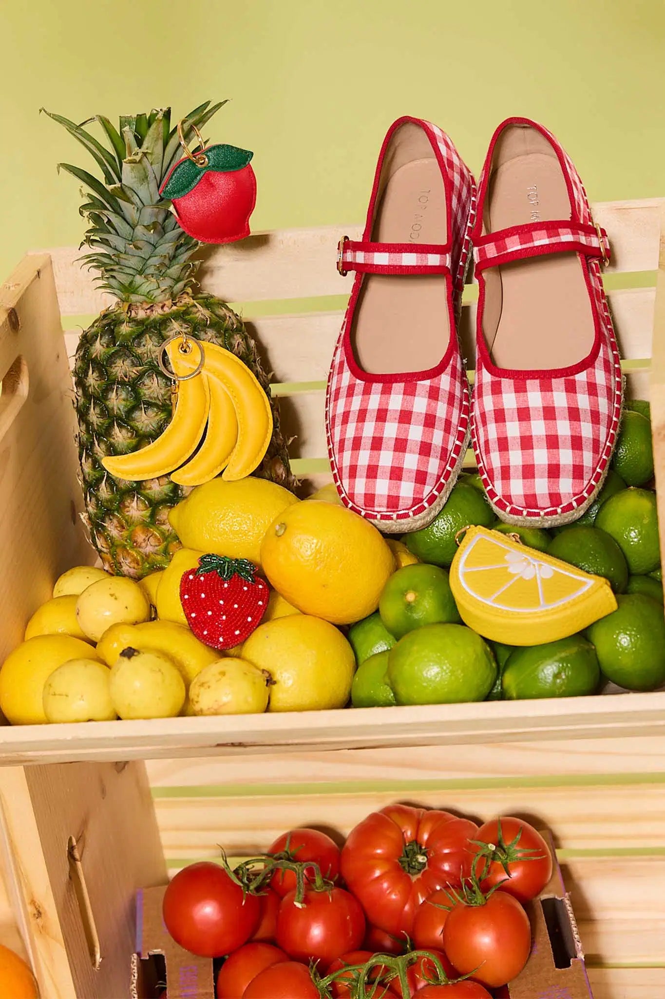 Red checkered shoes on a fruit and vegetable display with a pineapple, bananas, lemons, limes, strawberries, and tomatoes.