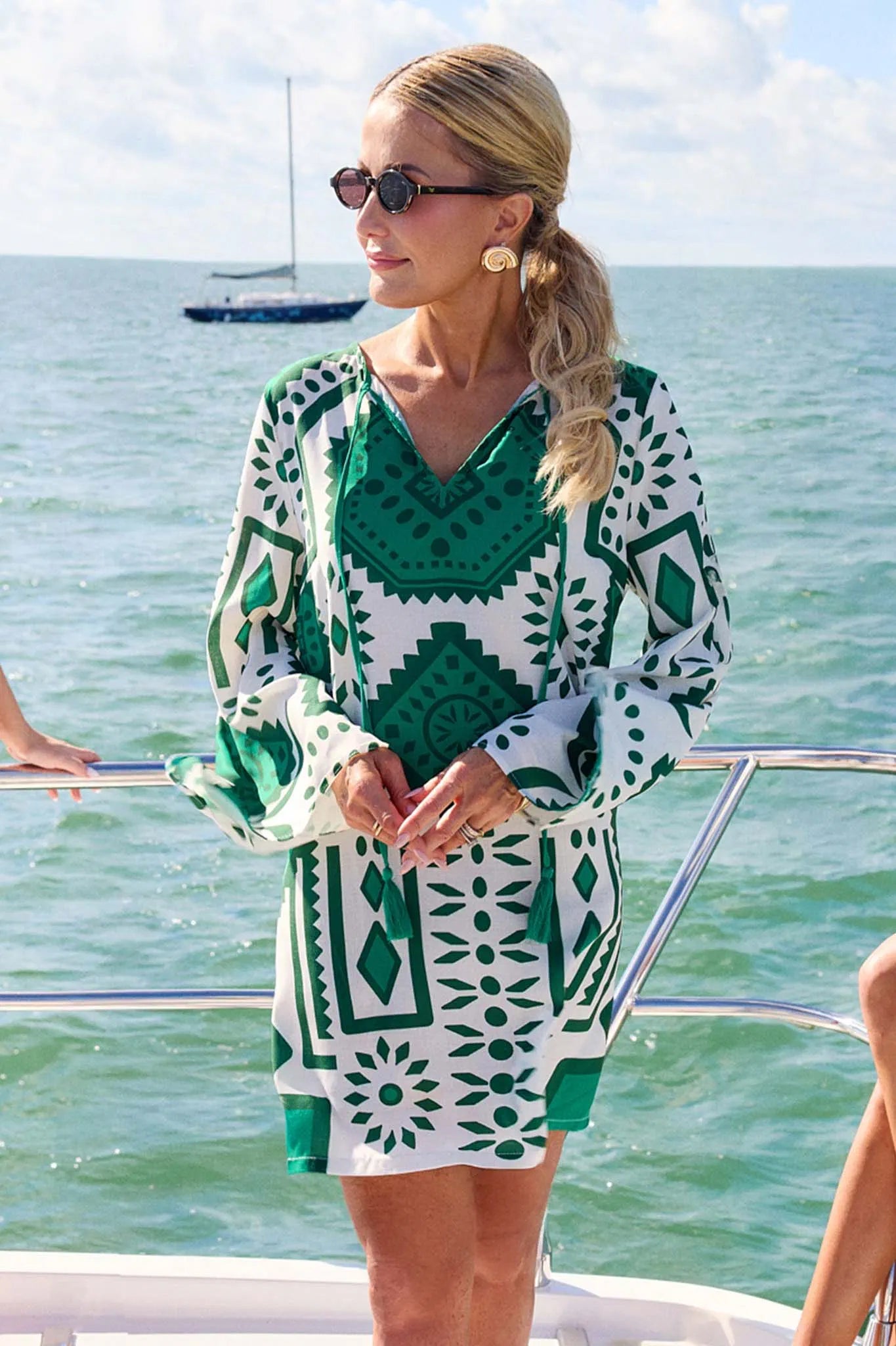 Woman in a green and white patterned dress on a boat with water and sky in the background