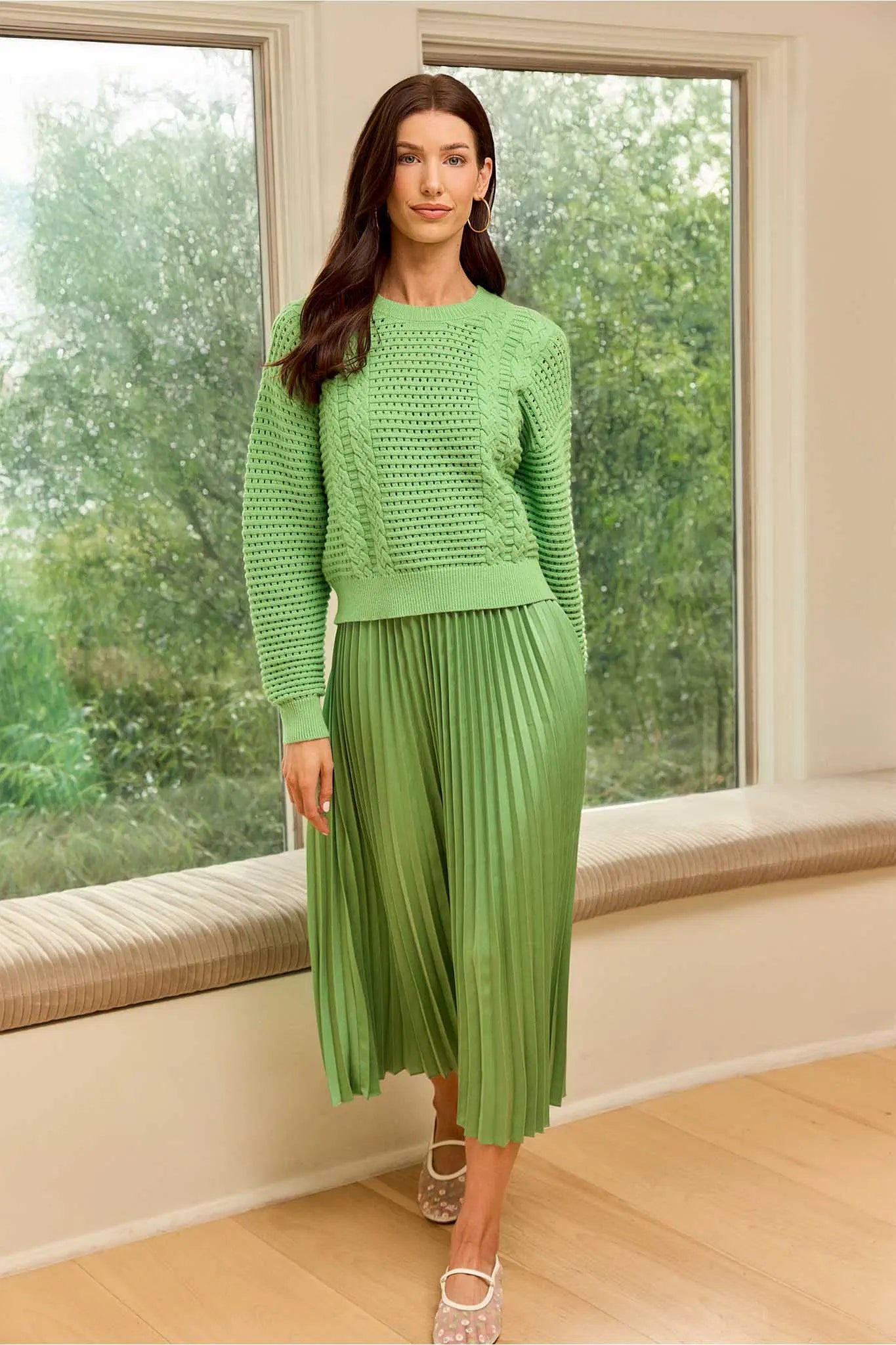 Woman wearing a green outfit standing in a room with large windows.