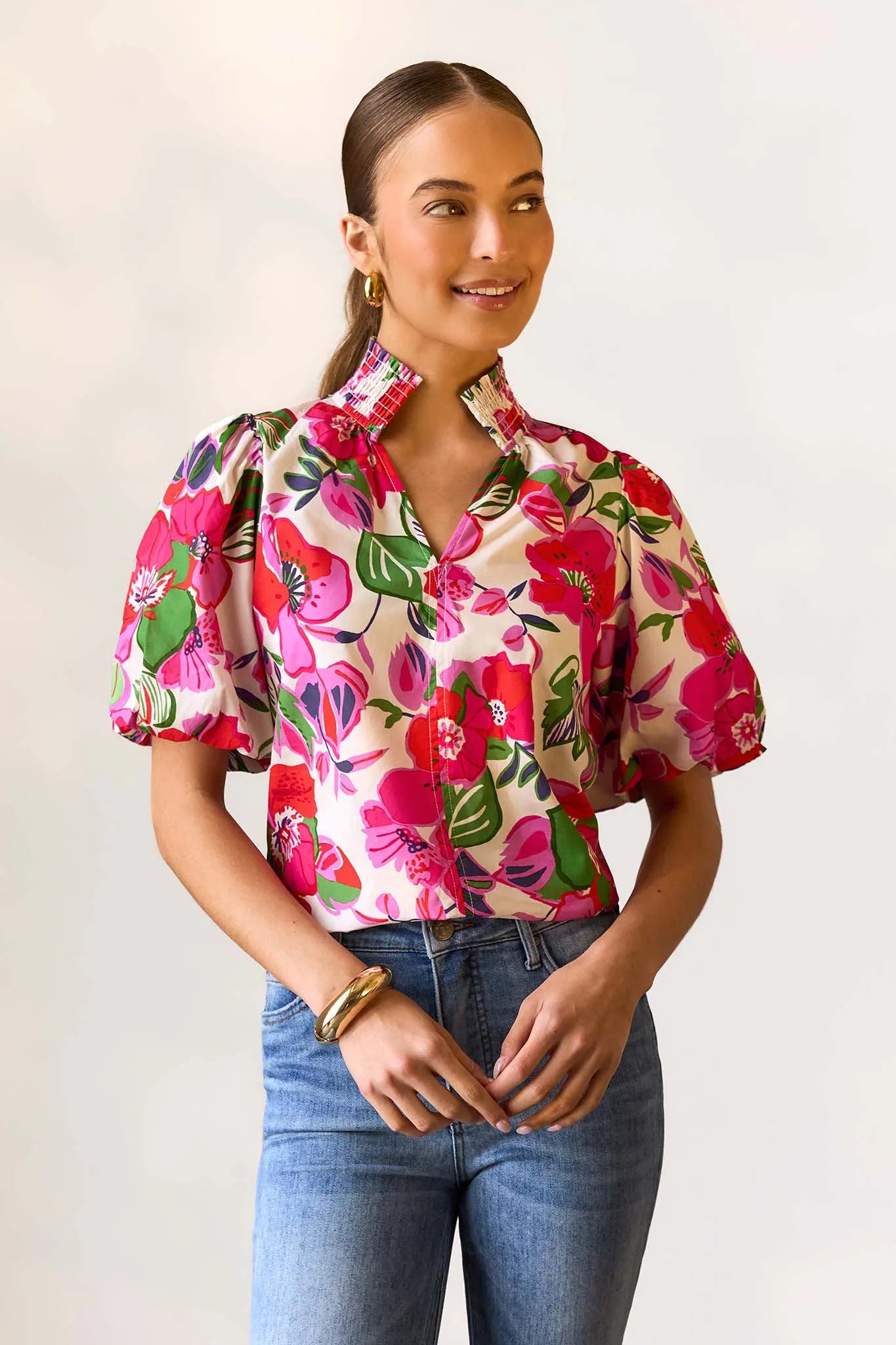Woman wearing a colorful floral blouse and blue jeans against a plain background
