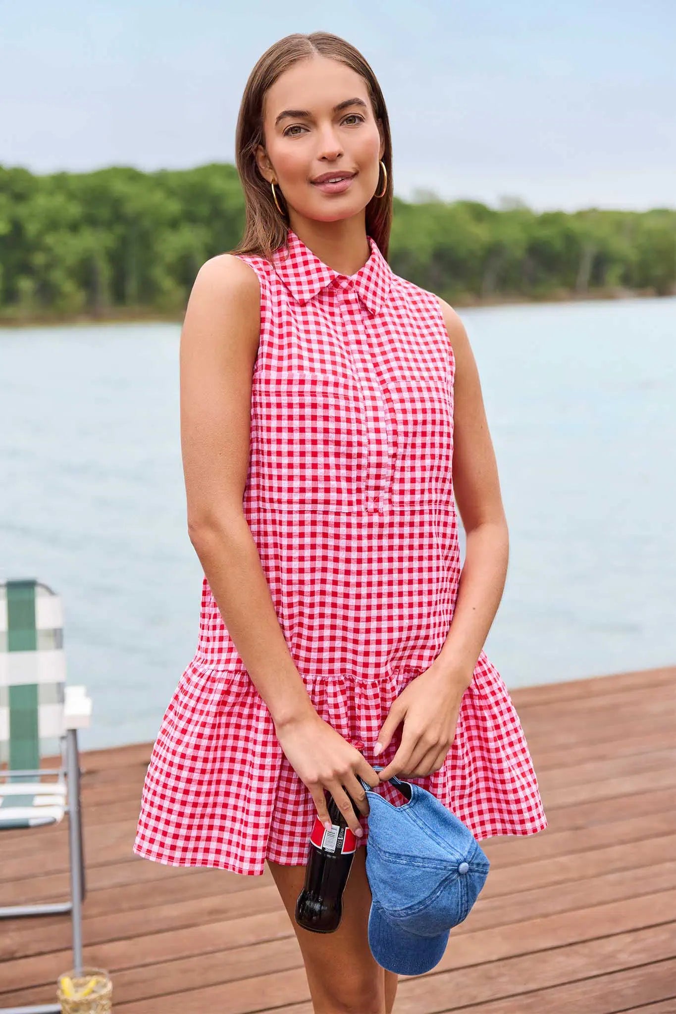 Woman in a red and white checkered dress standing on a dock by a lake.