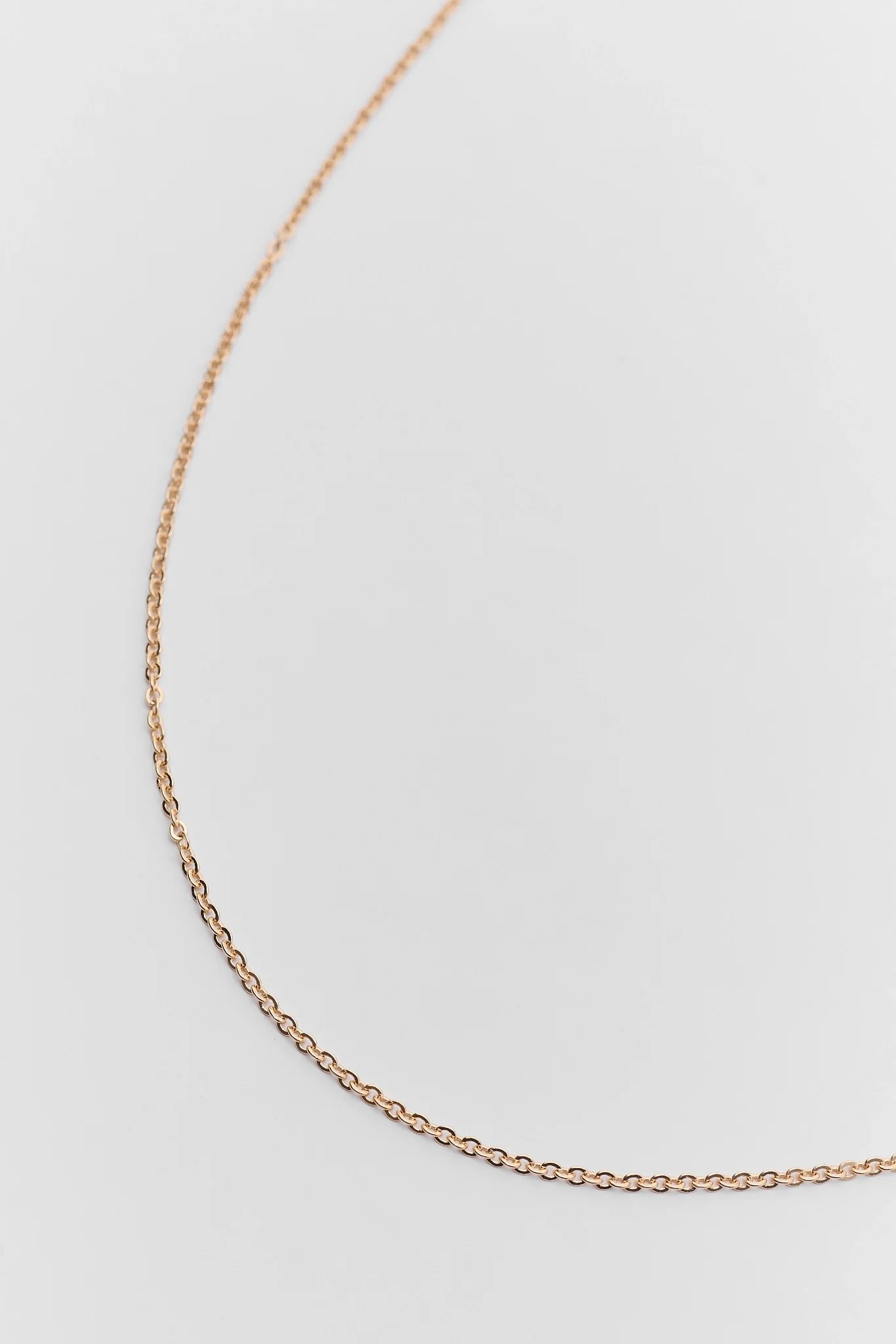 A delicate rose gold chain necklace draped in a gentle curve against a clean, light gray background.