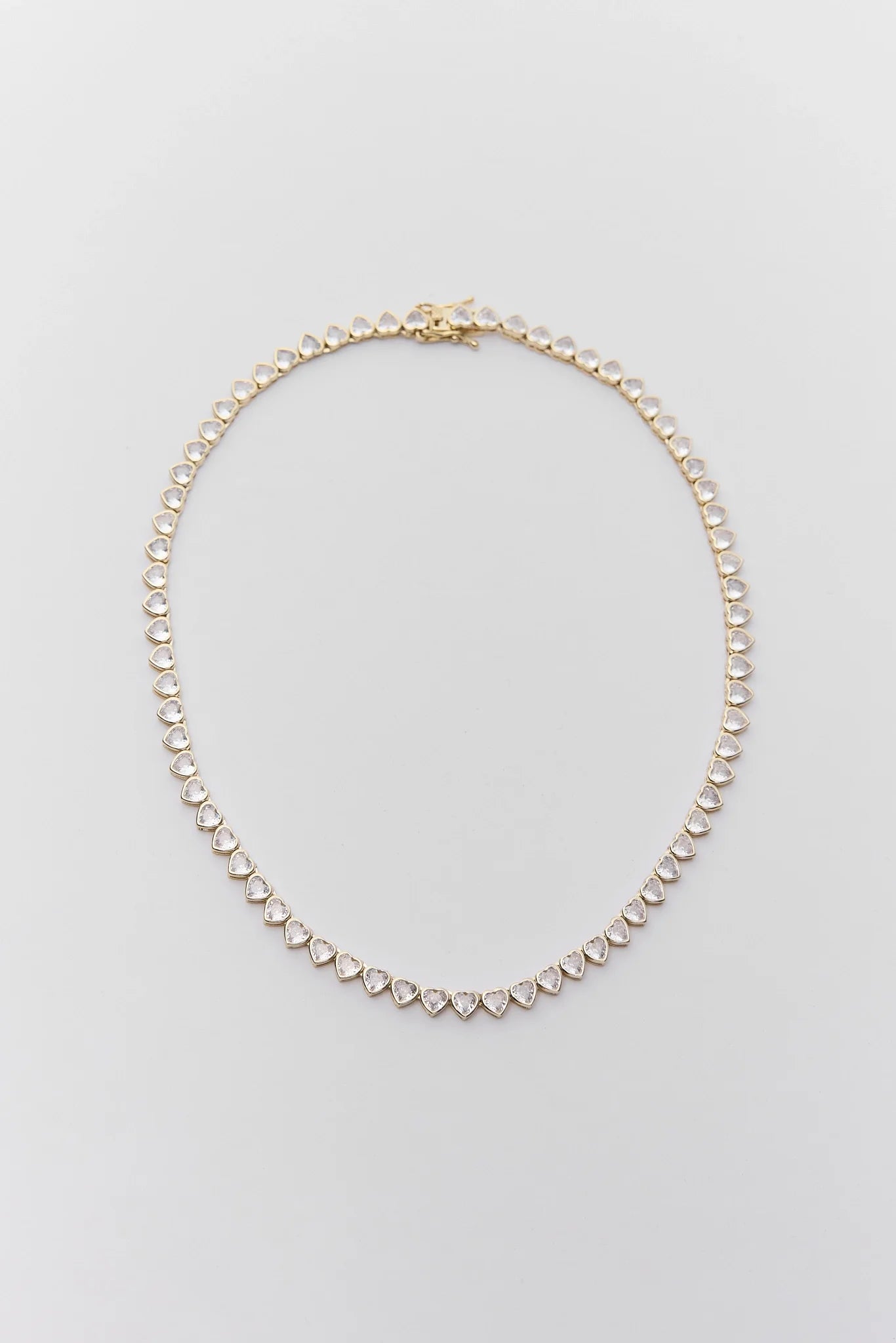A delicate gold chain necklace featuring small, clear heart-shaped pavé gemstones along the front, displayed on a clean, light gray background.
