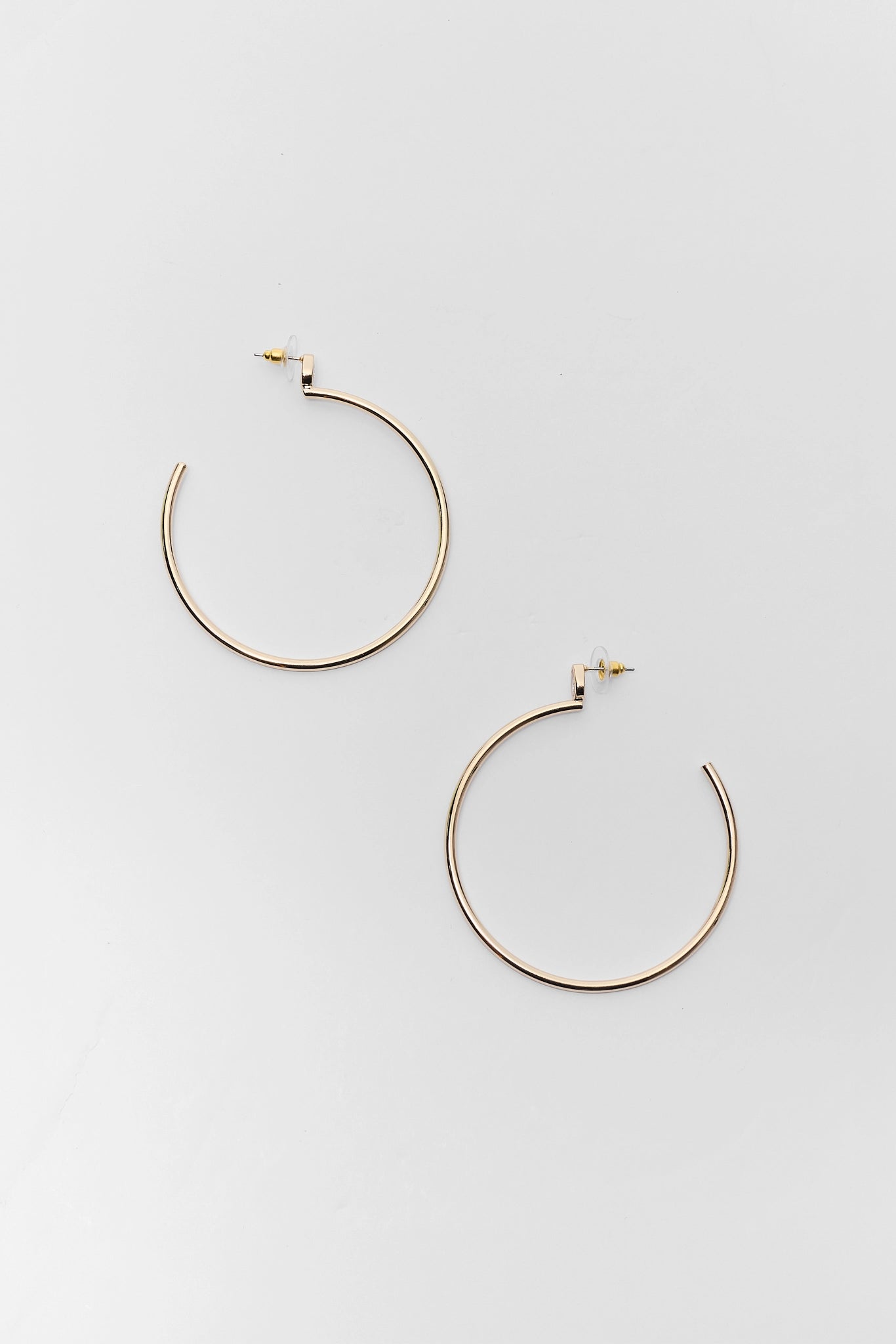 A pair of thin gold-tone hoop earrings with post backings, displayed on a clean, light gray background.
