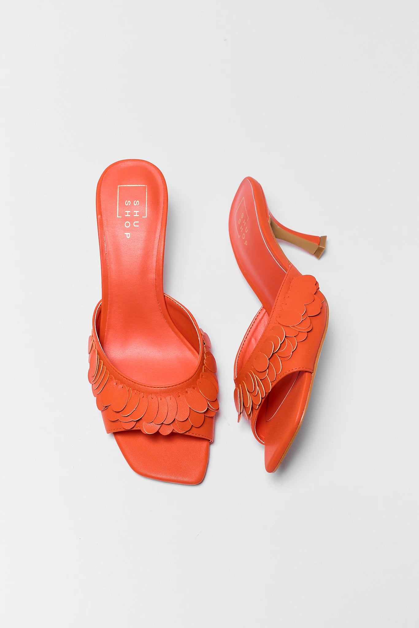 Pair of orange high-heeled shoes with scalloped edges on a light gray background